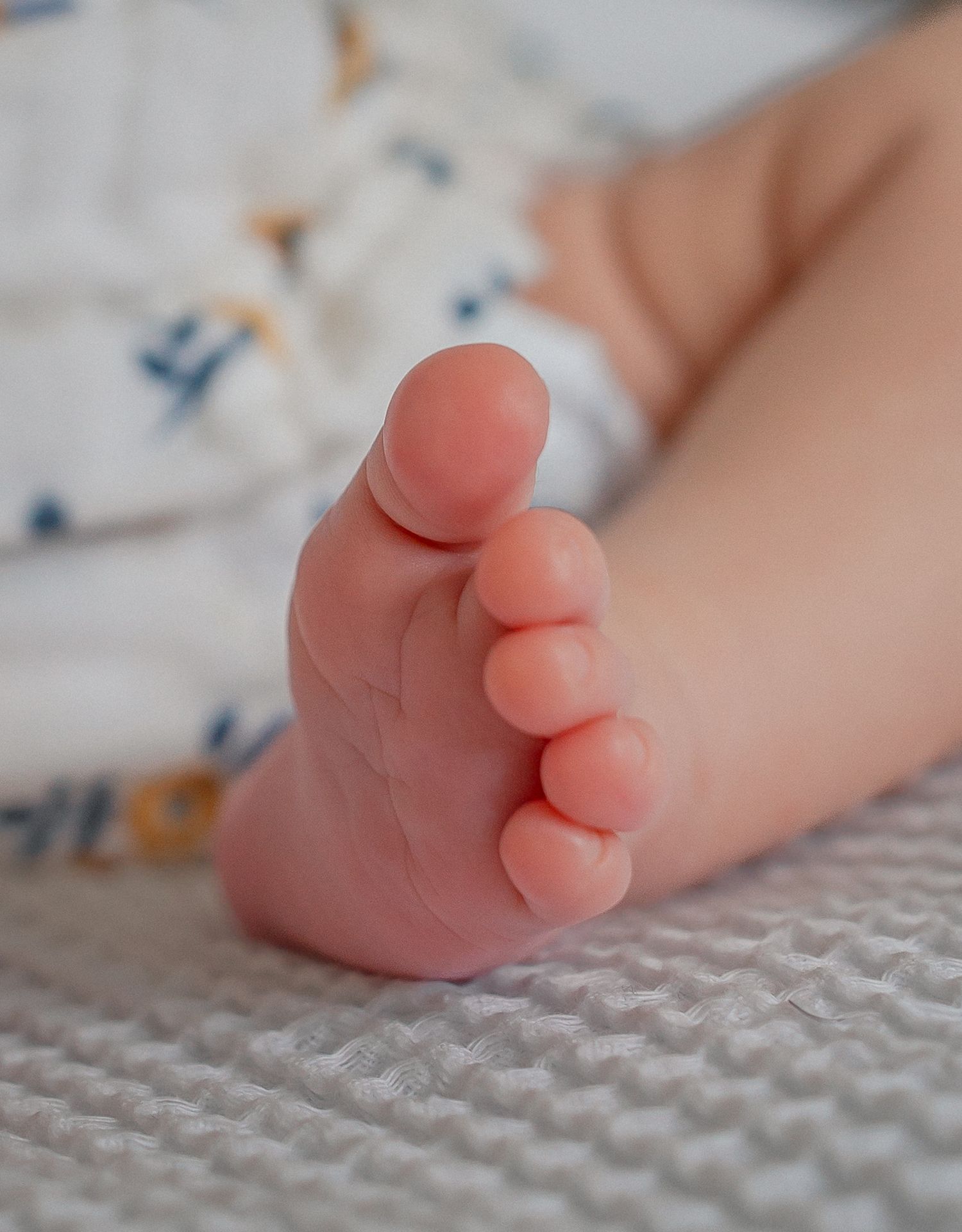 Close-up of a newborn baby's tiny foot with chubby toes resting on a white textured blanket in Chippenham.