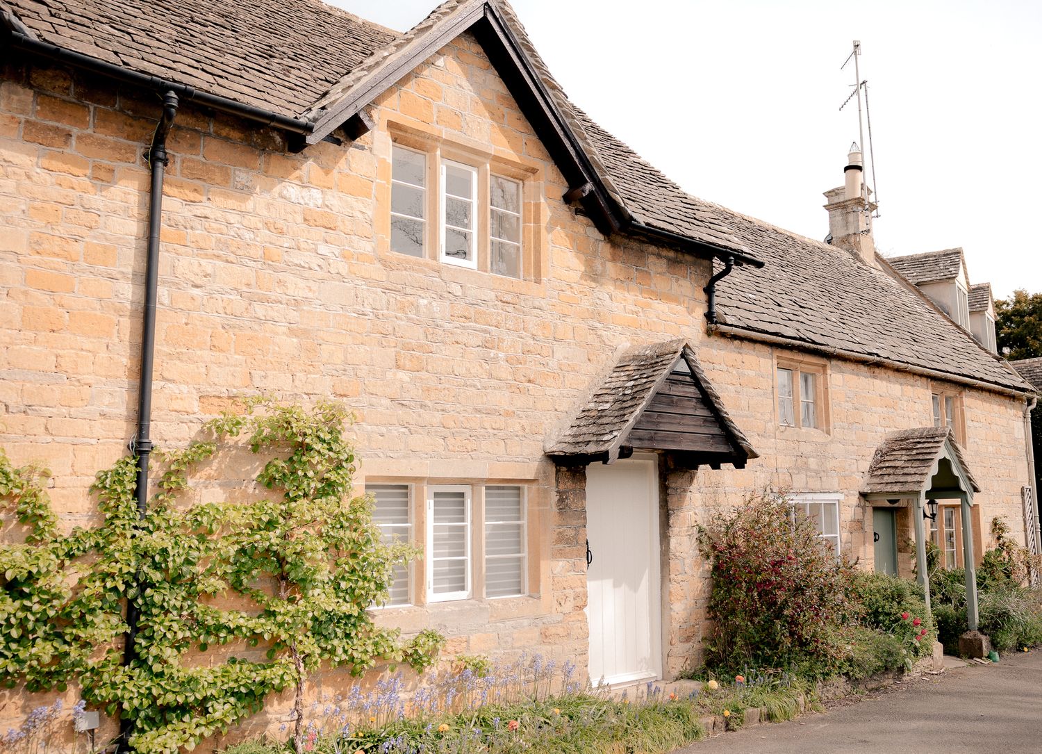 Charming Cotswold stone cottage with climbing plants, traditional English architecture on a quiet village street in Lower Slaughter.