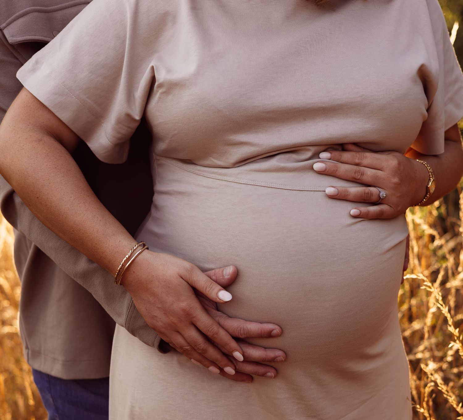 A close up photo of mum and dad to be showing off a pregnant belly during golden hour lighting. River Bybrook