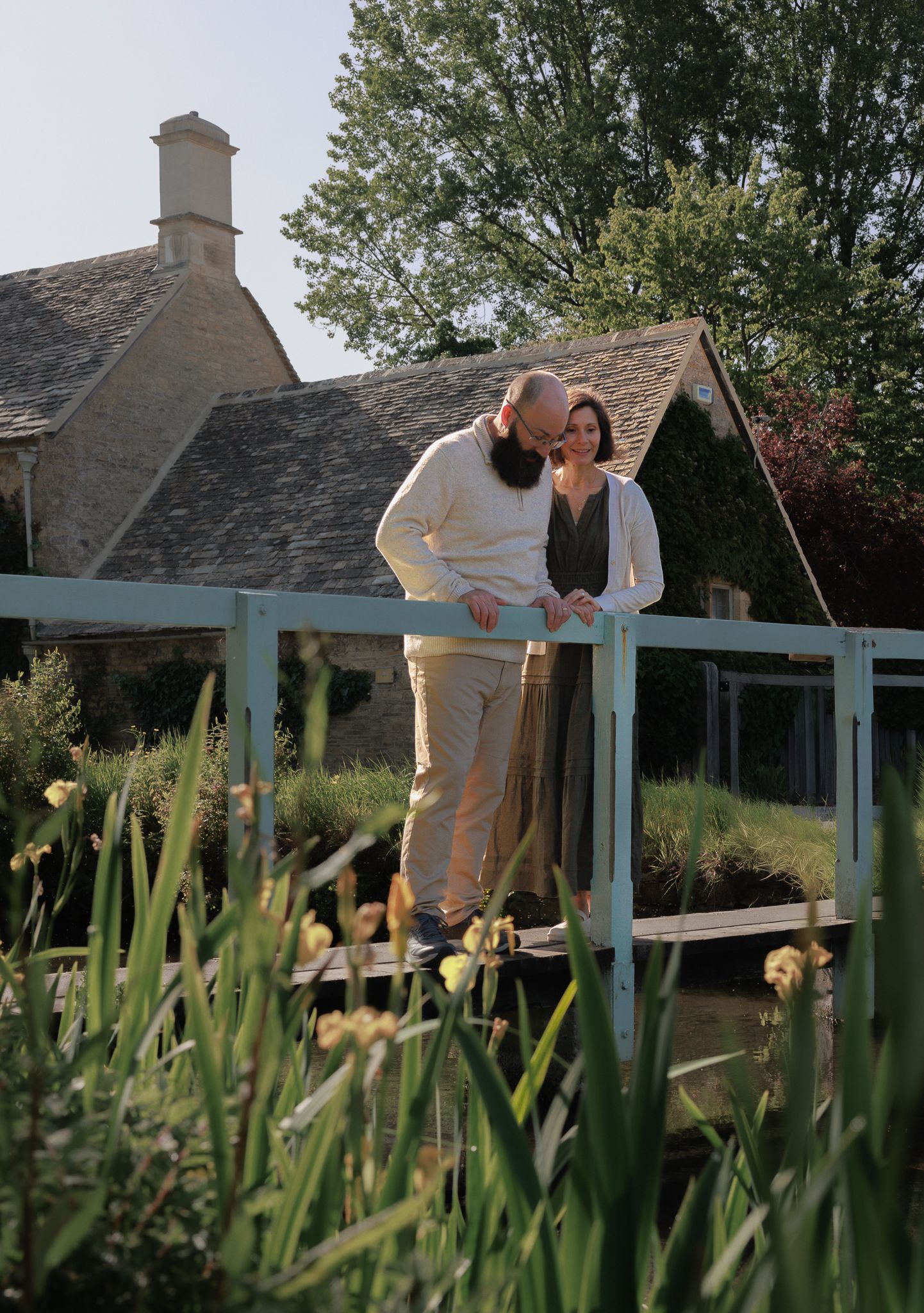 A couple shares a romantic moment on a rustic blue bridge surrounded by lush garden greenery.