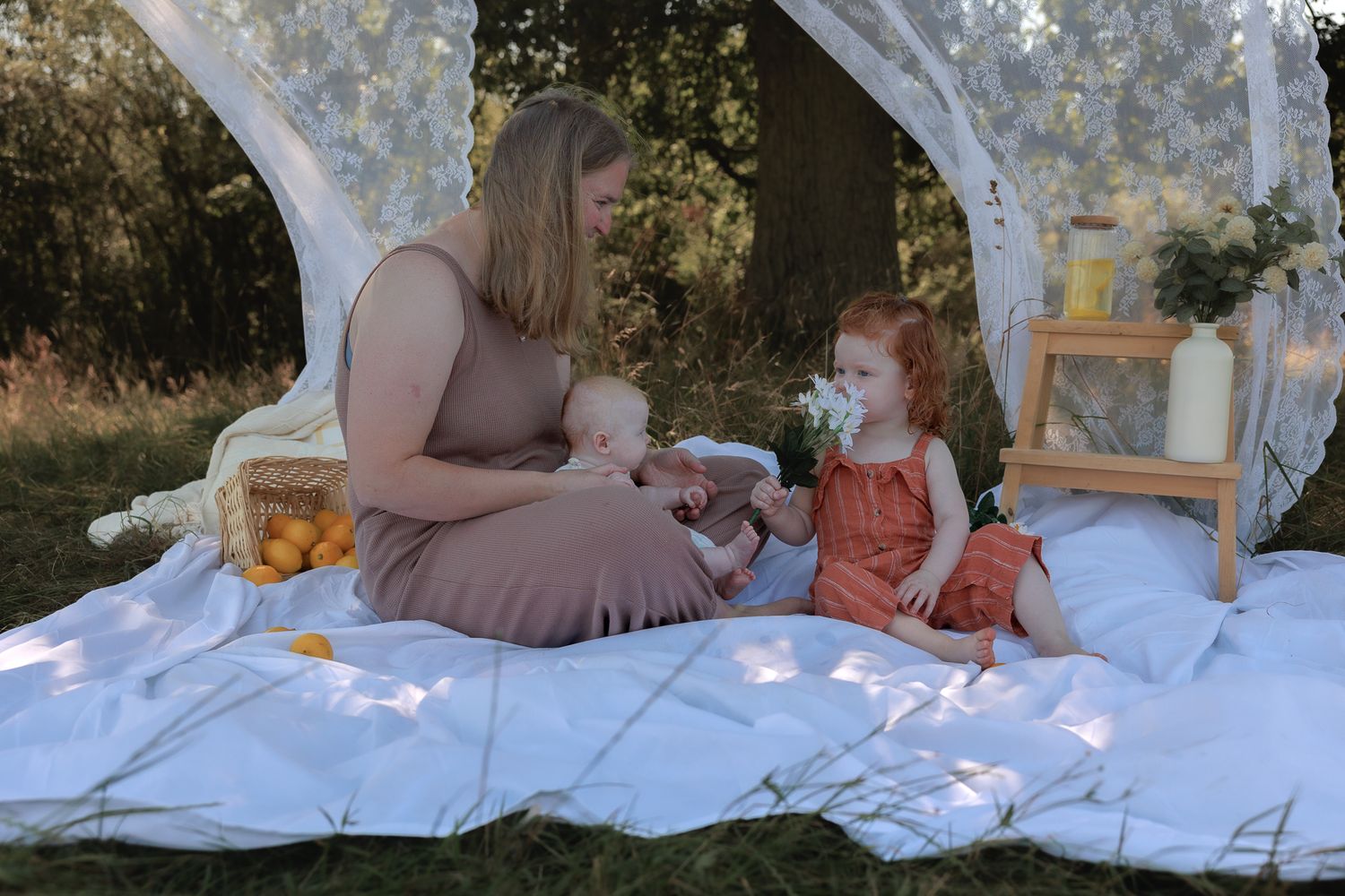 A mother sits on a white blanket outdoors with two young children during a peaceful picnic photo session in Henley-on-Thames, Oxfordshire.