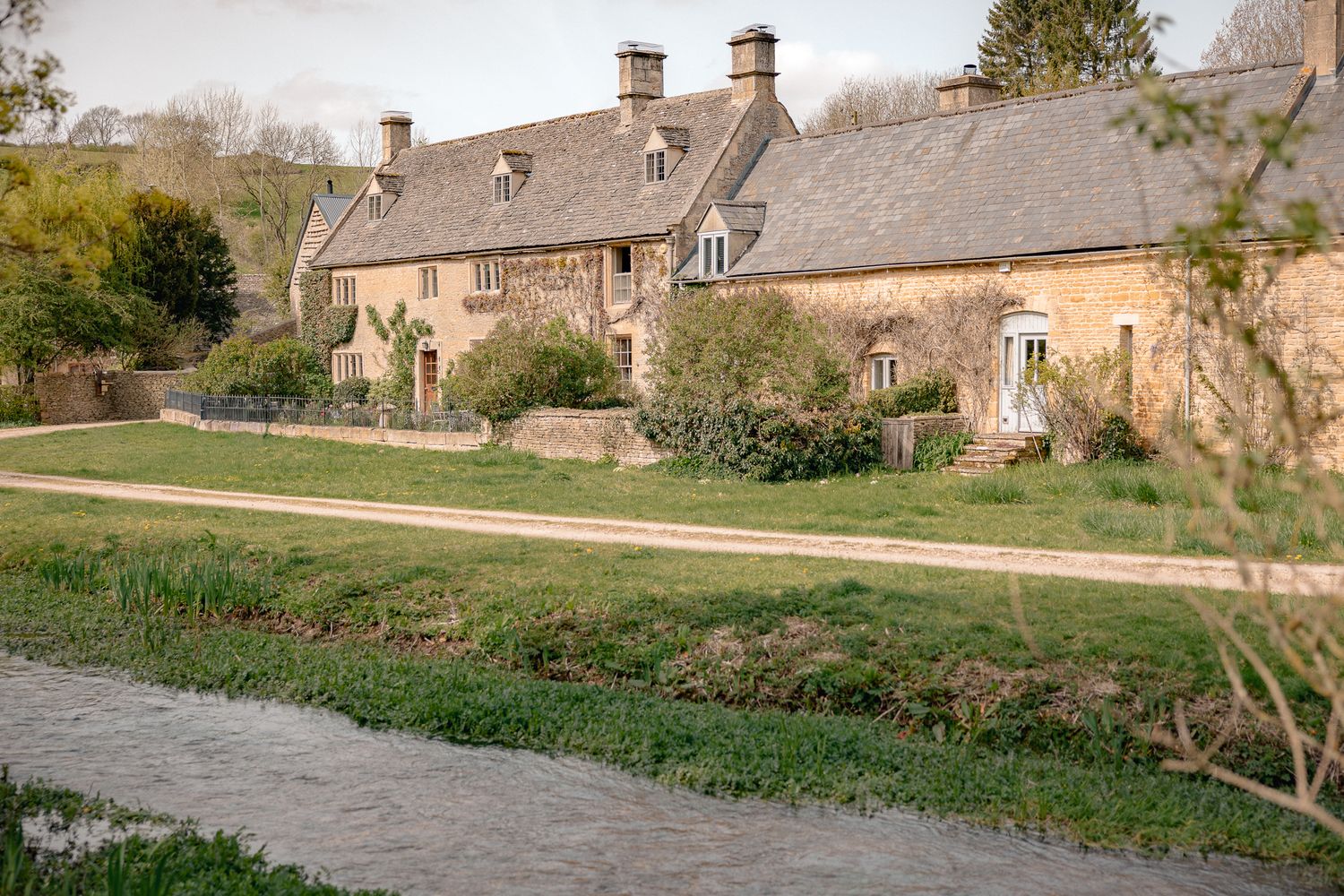 Charming Cotswold stone cottages beside a peaceful stream with lush green gardens in an English village in Upper Slaughter, Cotswolds, UK.