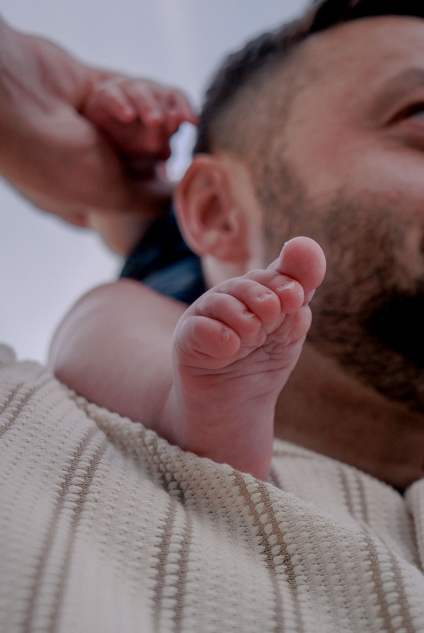 Close-up of a newborn baby's tiny foot resting on a father's chest in Stow, Cotswolds.