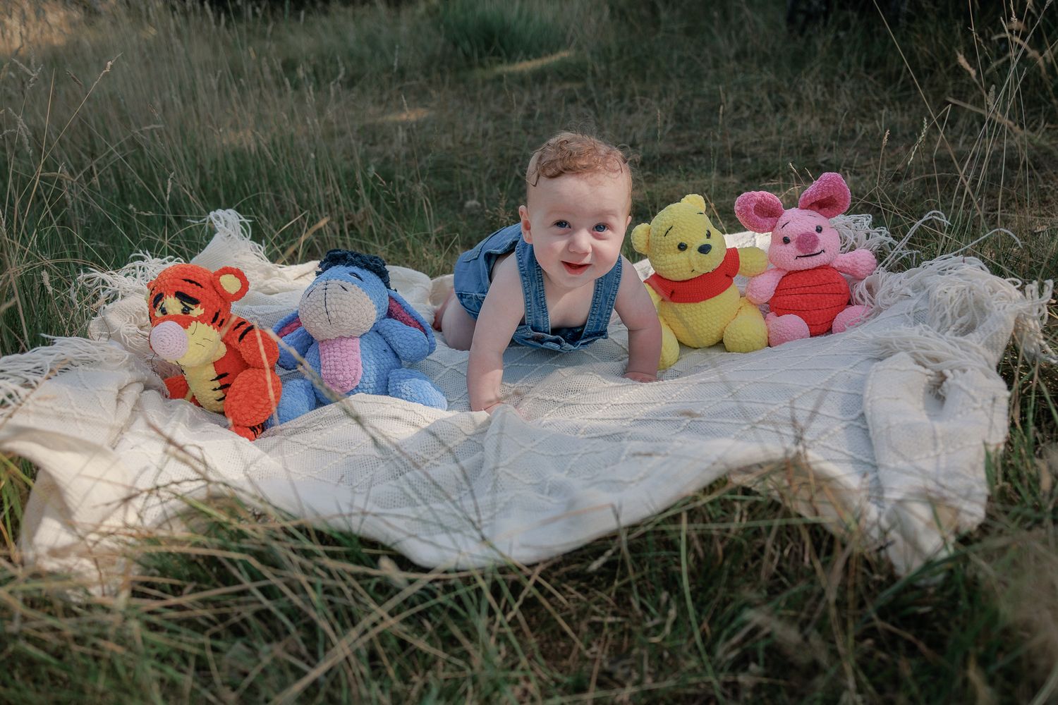Baby smiling on blanket outdoors surrounded by Winnie the Pooh stuffed animals in Burford, Cotswolds.