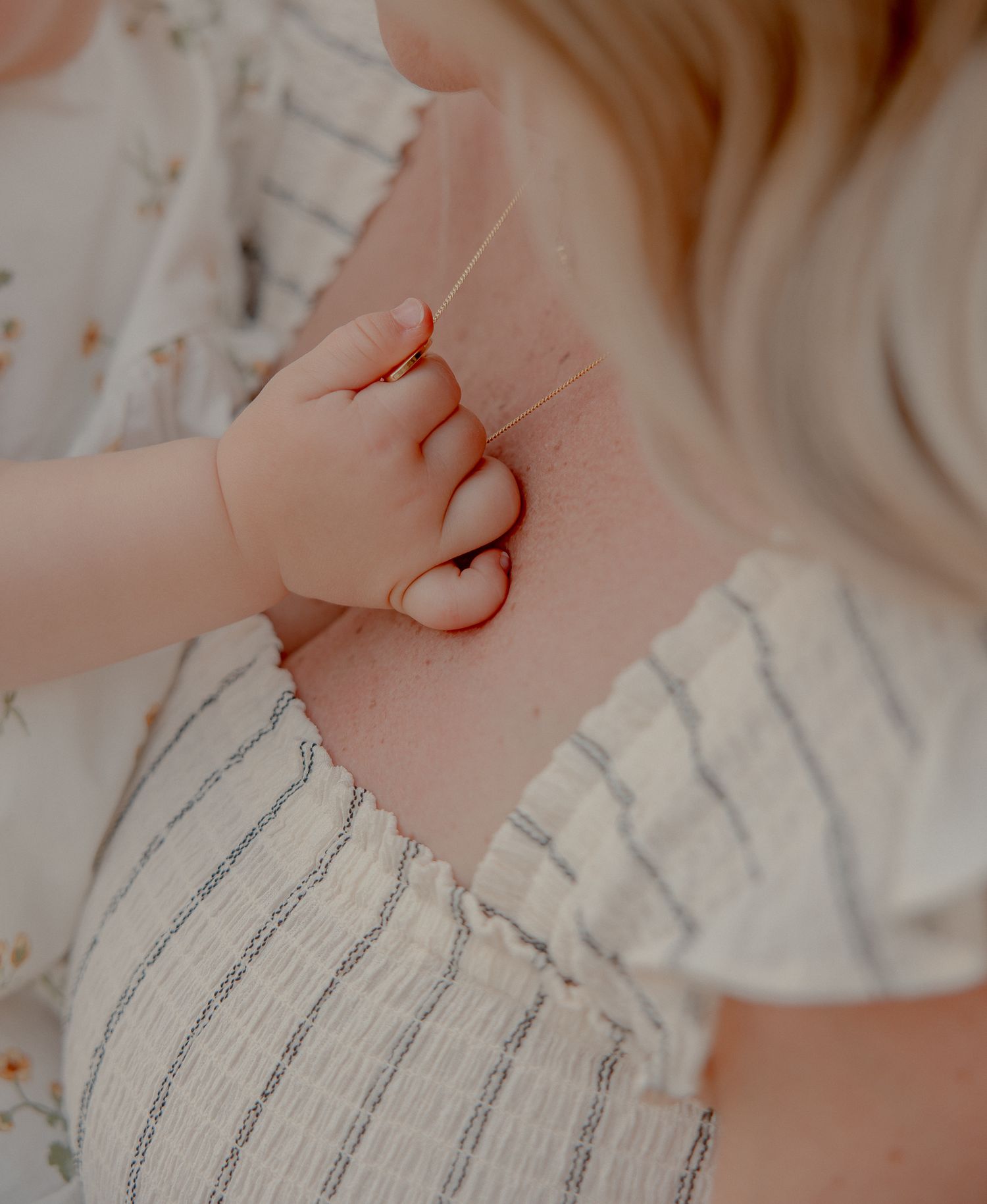 A baby's tiny hand gently gripping an adult's back, both wearing soft white clothing in a tender moment.