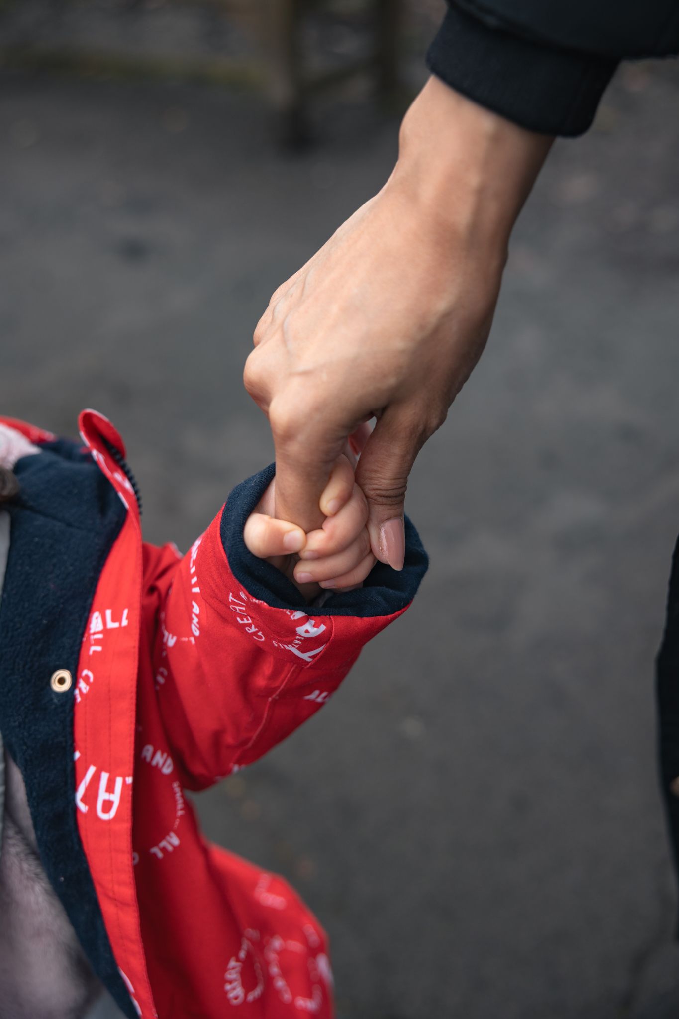 Adult hand gently holding a small child's hand, child wearing a red jacket, in North Cerney, Cotswolds.