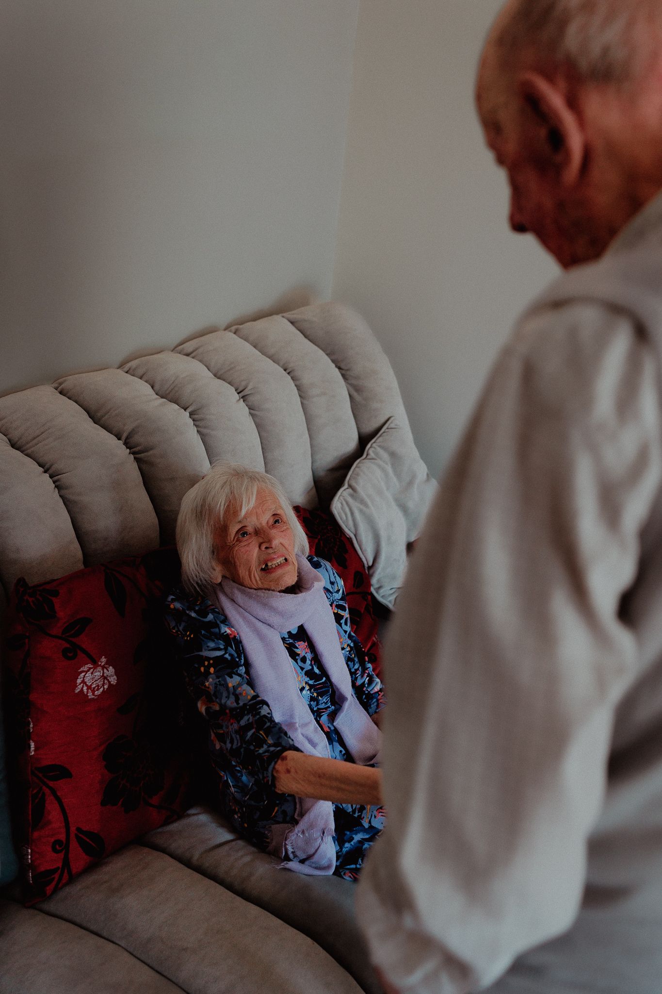 Elderly woman smiling warmly at an older man while sitting on a cosy sofa in Chipping Norton.