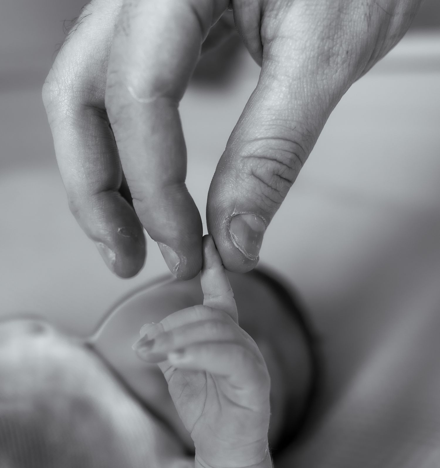 Black and white photo of an adult hand gently holding a tiny newborn baby's finger during Newborn Photoshoot in Biddestone.