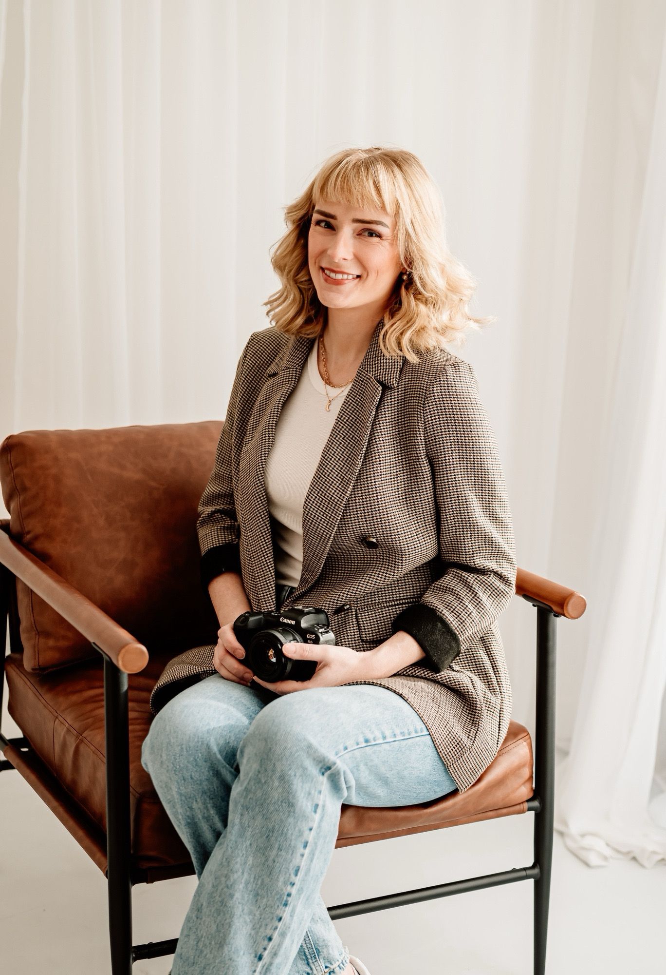 Tasha Dowse Photography sits in a gray blazer and jeans sits casually on brown leather chair during photoshoot in Bathampton, Somerset.