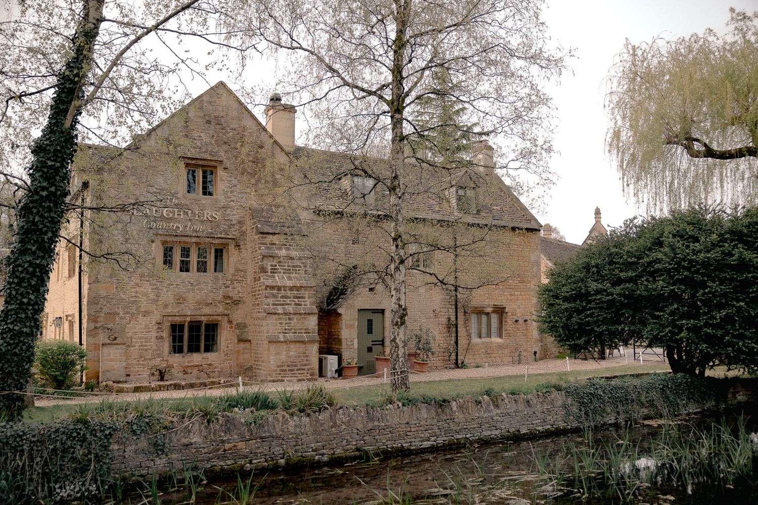 Historic Cotswold stone manor house with ivy-covered walls beside a tranquil stream, The Slaughters Country Inn.