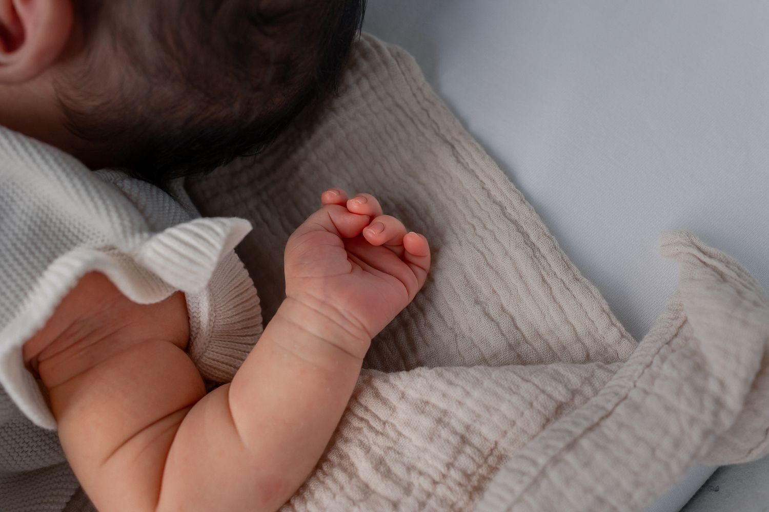 Close-up of a sleeping newborn baby's tiny hand and fingers resting on a soft textured blanket taken by a Cotswold Photographer in Bathford.
