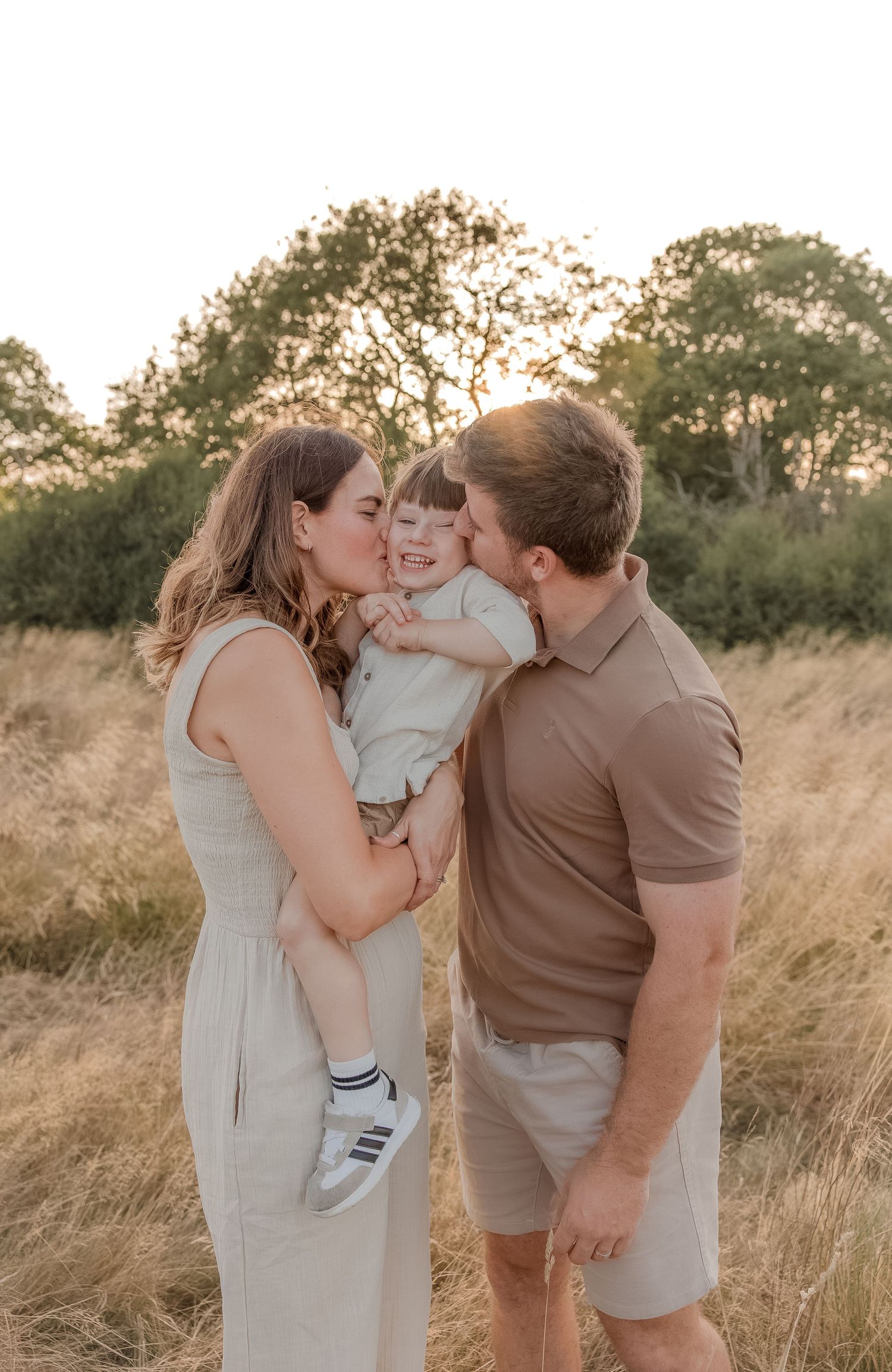 A couple kisses their smiling toddler during family photoshoot with Tasha Dowse Photography in Snowhill, Cotswolds.