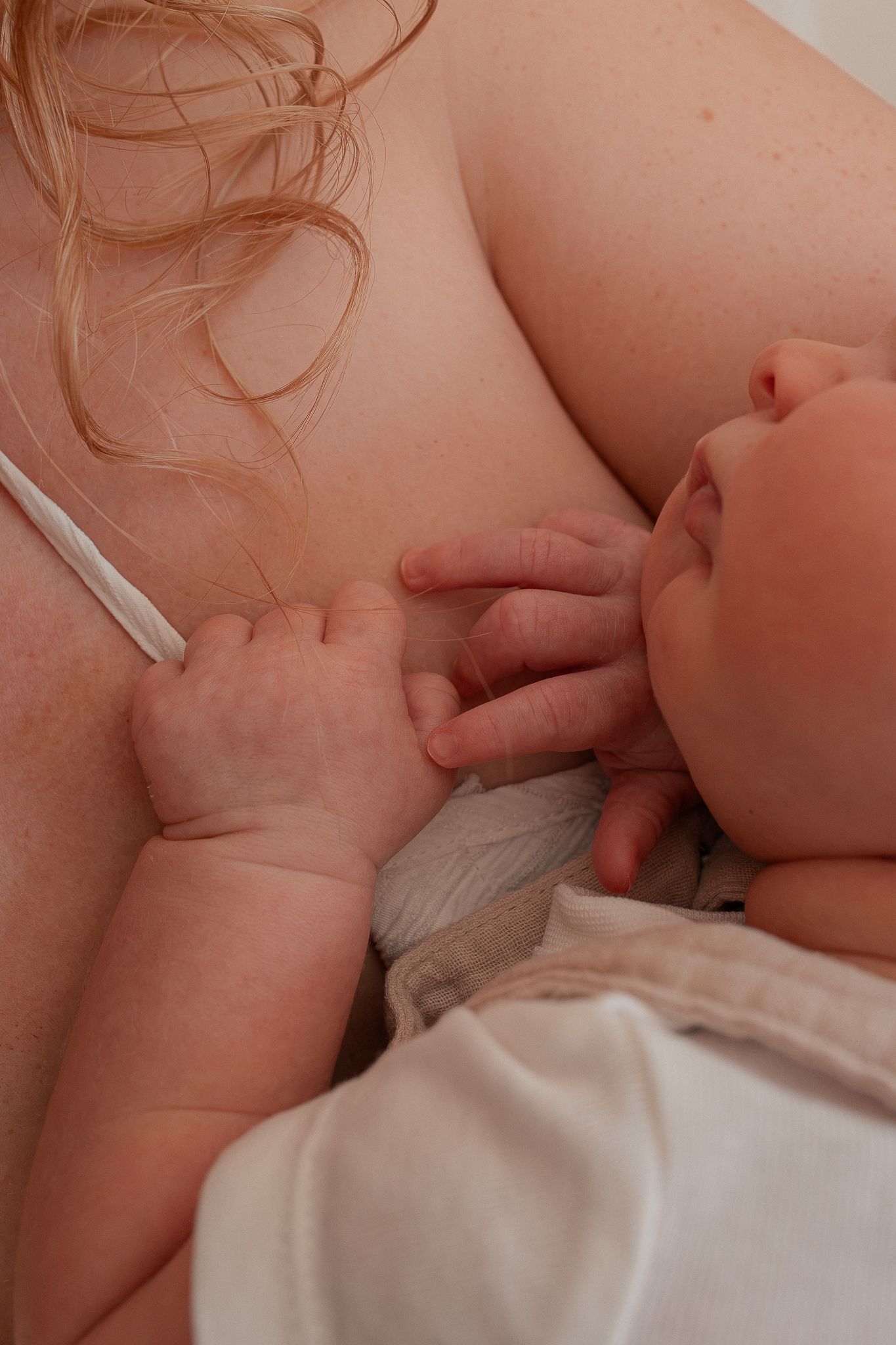 A newborn baby breastfeeding, gently resting tiny hands against mother's chest during nursing in Clevedon, North Somerset.