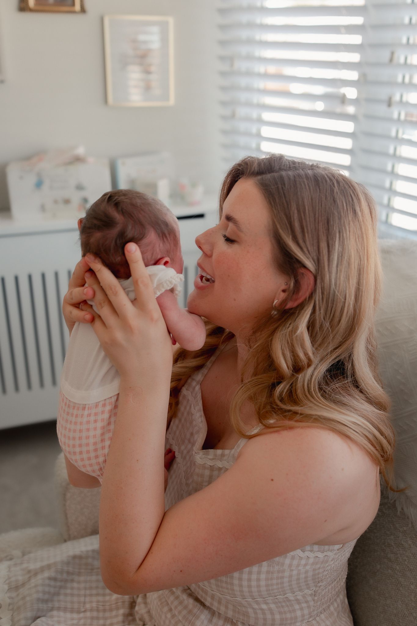 A mother lovingly holds her newborn baby up close to her face in a bright, softly decorated nursery room for a Newborn Photoshoot in Wellow.