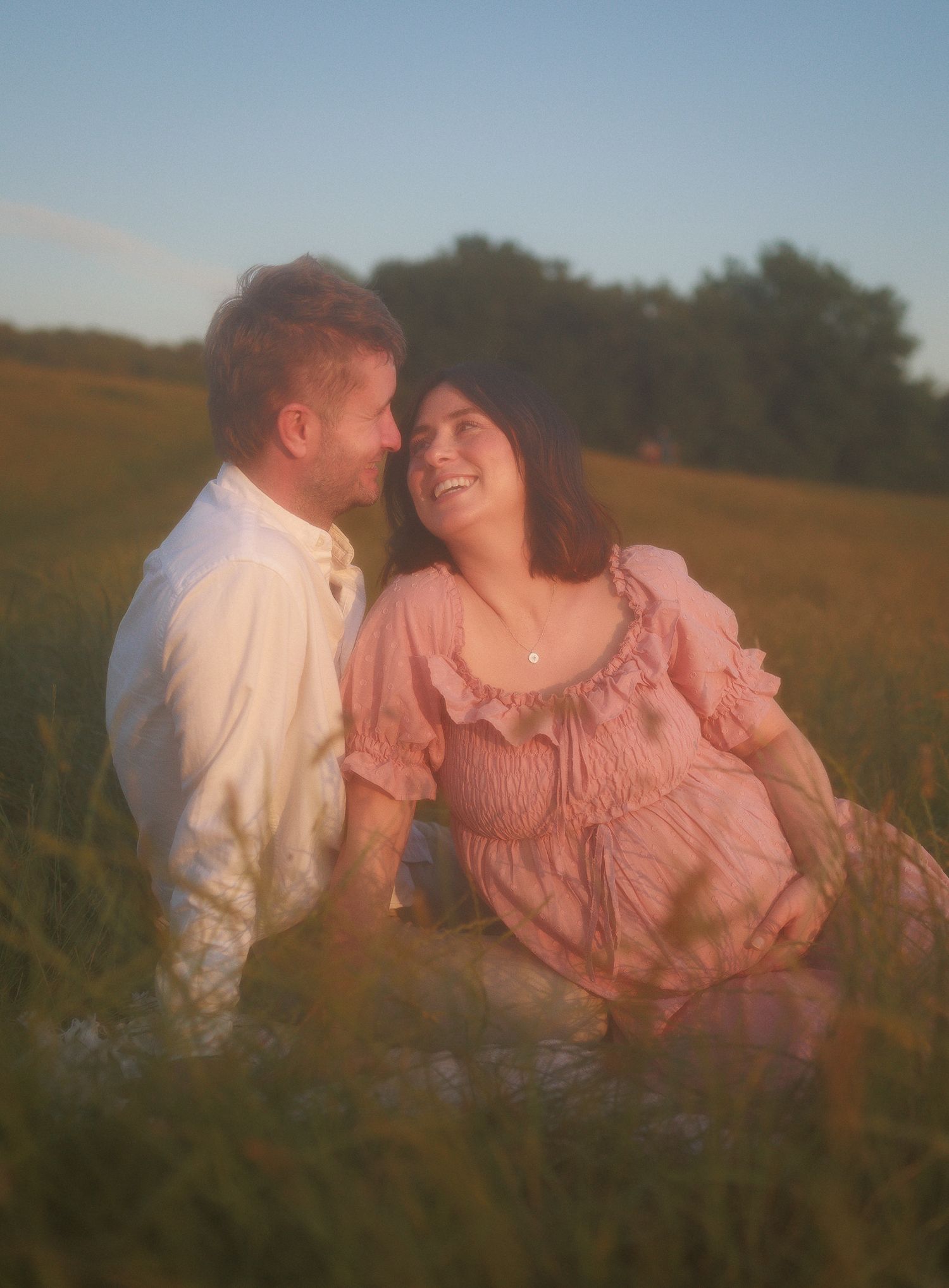 Couple sharing tender moment in green meadow at golden hour, for Maternity Photoshoot in Bathwick.