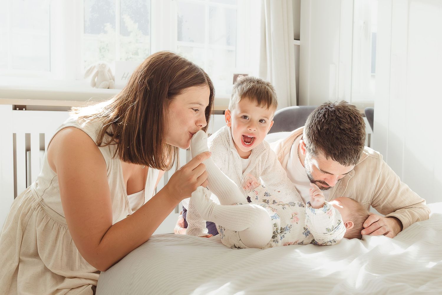 Family Photographer takes photo of family with two children bonding on a white bed in Bibury, Cotswolds.
