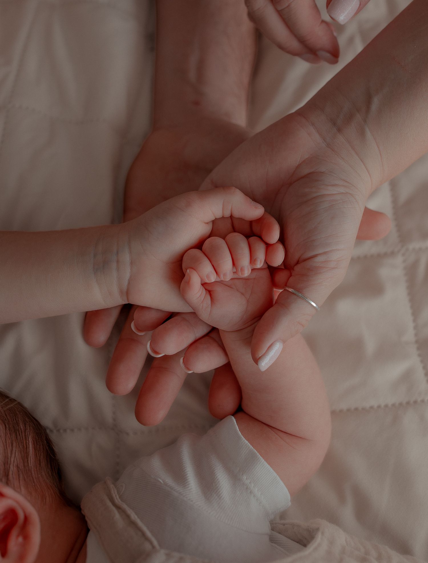 A newborn baby's tiny hand grasping an adult's finger, cradled gently in a parent's palm on a white blanket in Clifton, Bristol.
