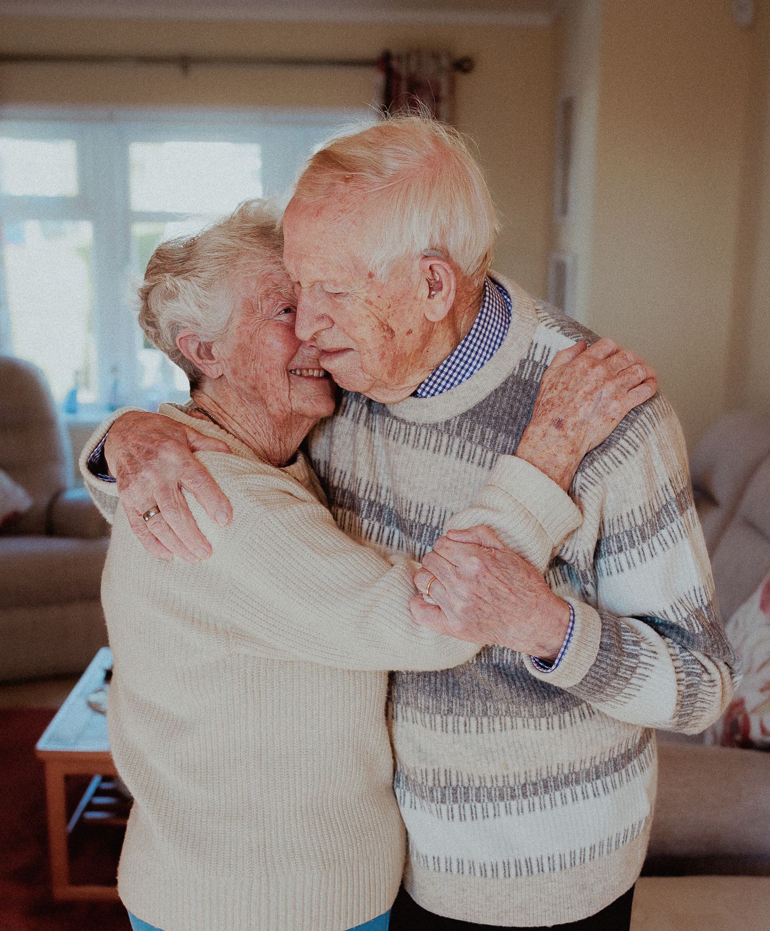 An elderly couple share a tender embrace while hugging in their living room in Knightsbridge.