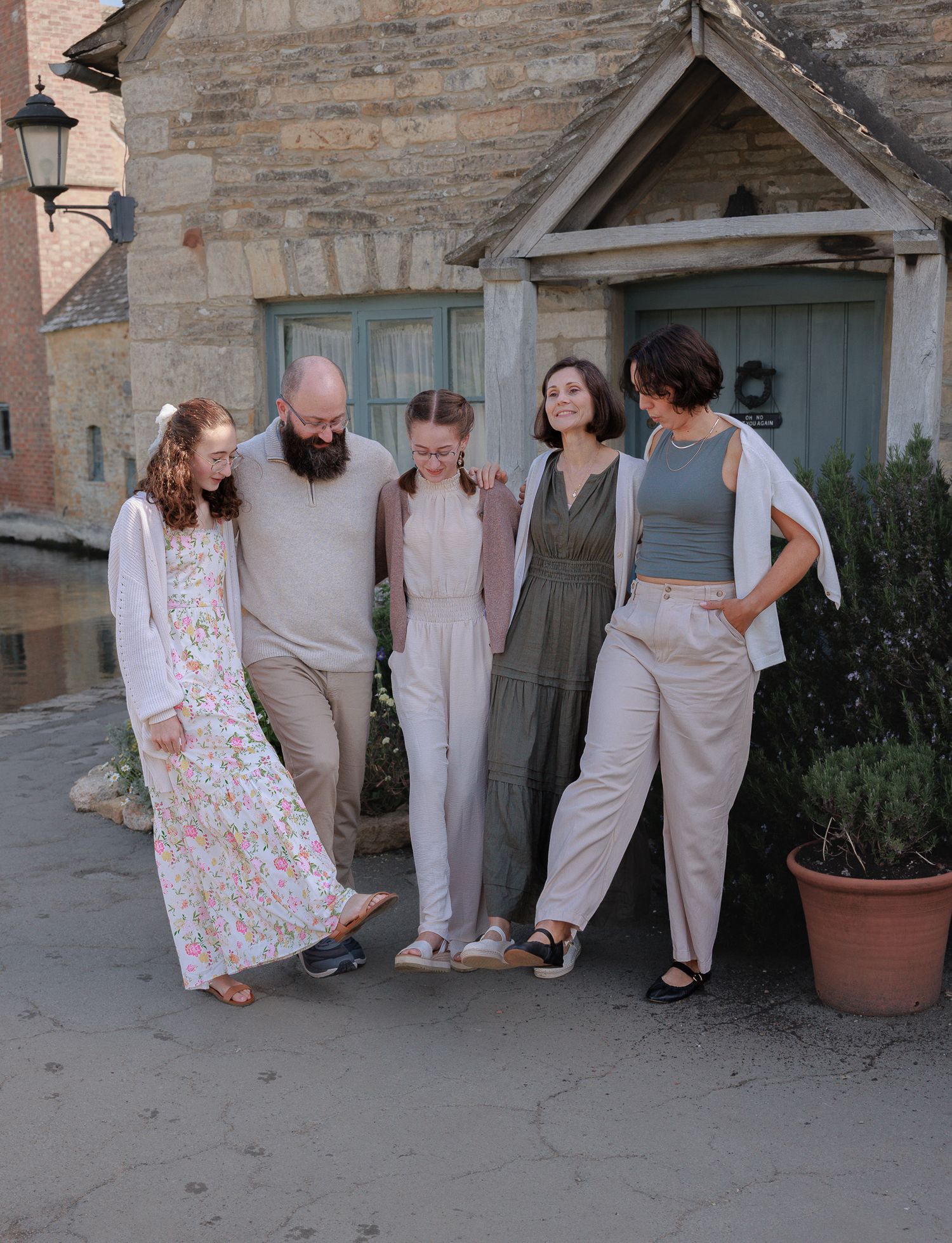 A happy family of five laughs together outside a rustic stone building in the Cotswolds.