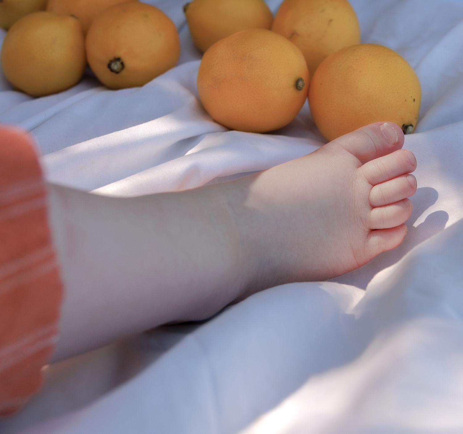 Close-up of a baby's foot resting on white fabric surrounded by fresh yellow lemons and oranges in Henley-on-Thames, Oxfordshire.
