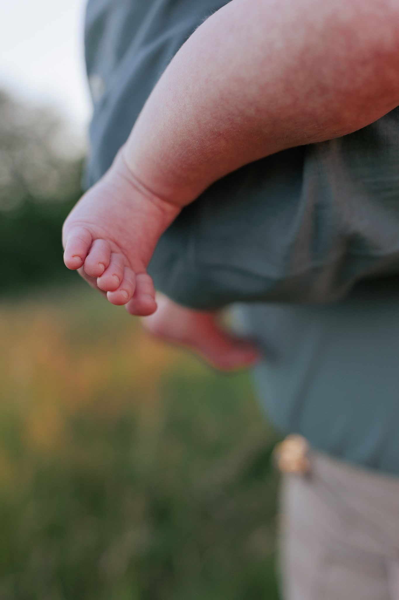 Close-up of tiny newborn baby feet resting on an adult's arm outdoors in soft natural light in Fairford.