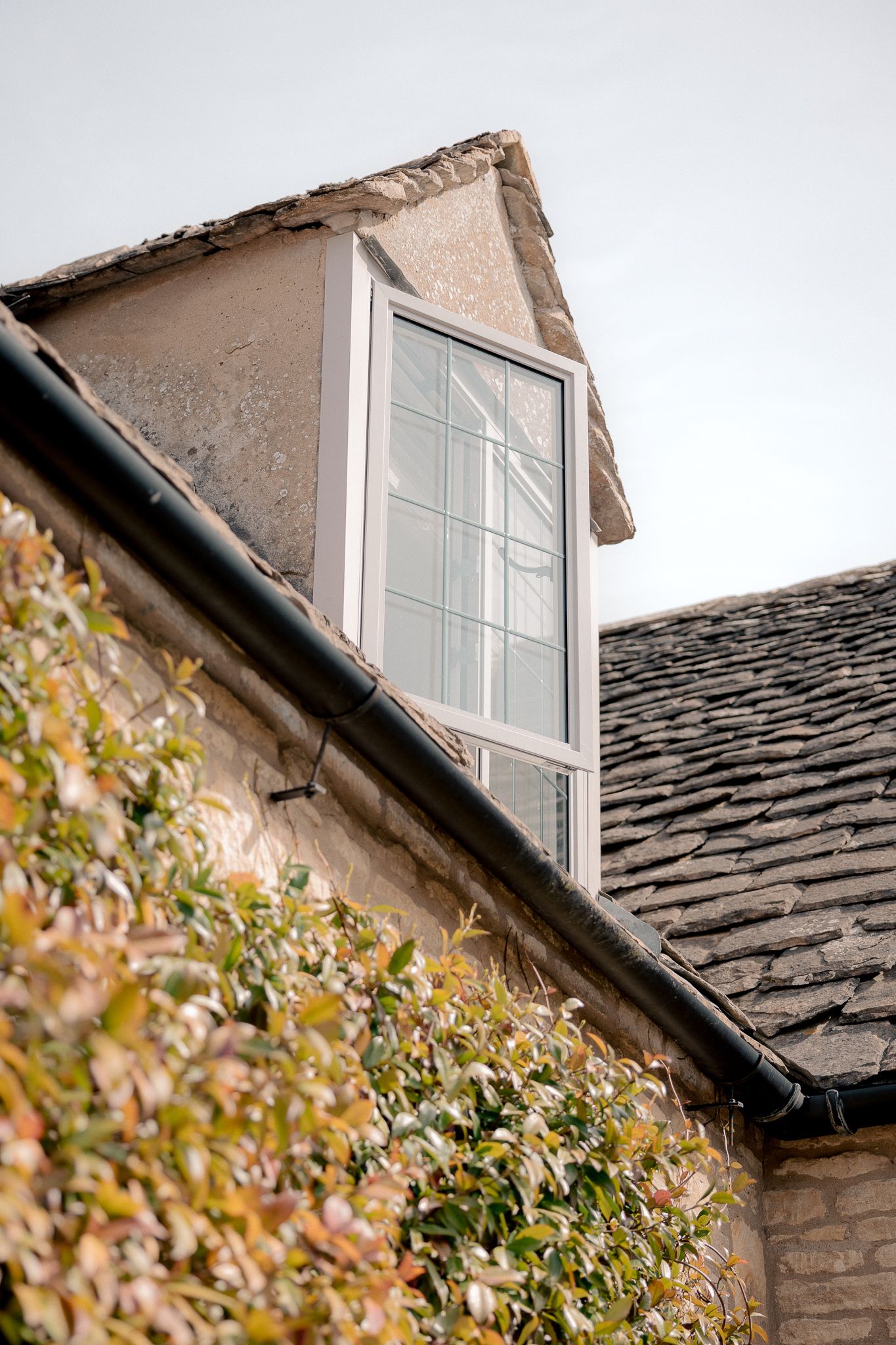 Stone cottage dormer window with white frame, ivy-covered walls,  in Lower Slaughter, Cotswolds, UK.