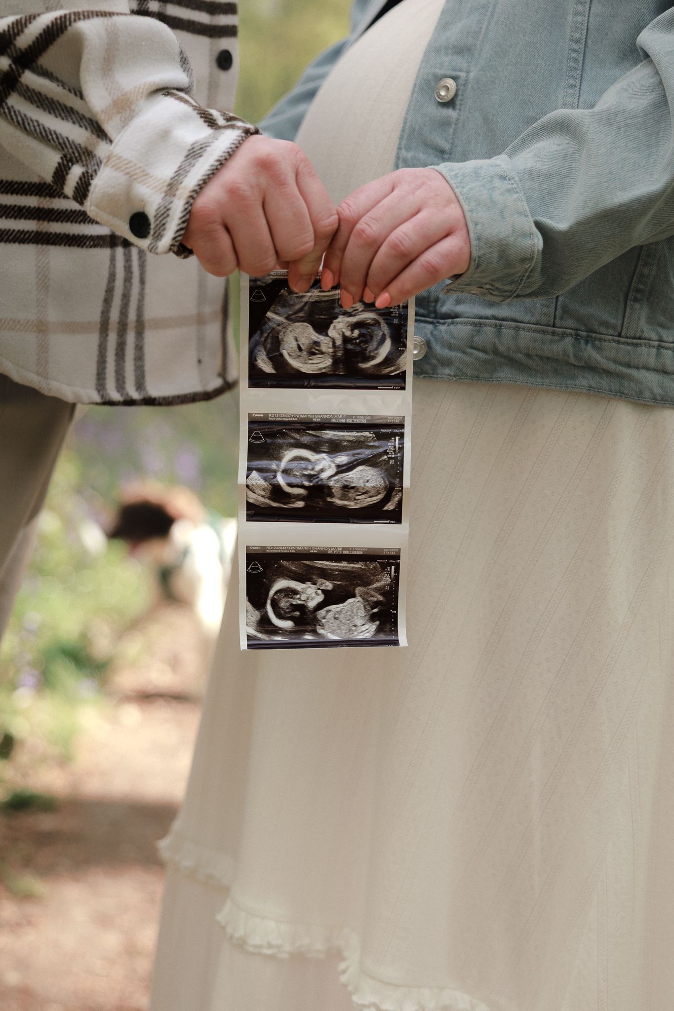 Pregnant woman and partner holding ultrasound photos outdoors, showing baby sonogram images during pregnancy announcement.