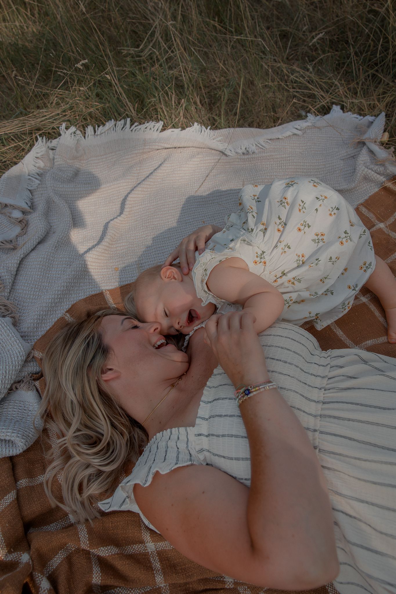 A mother and baby lying on a plaid blanket in a field, sharing a tender moment together.