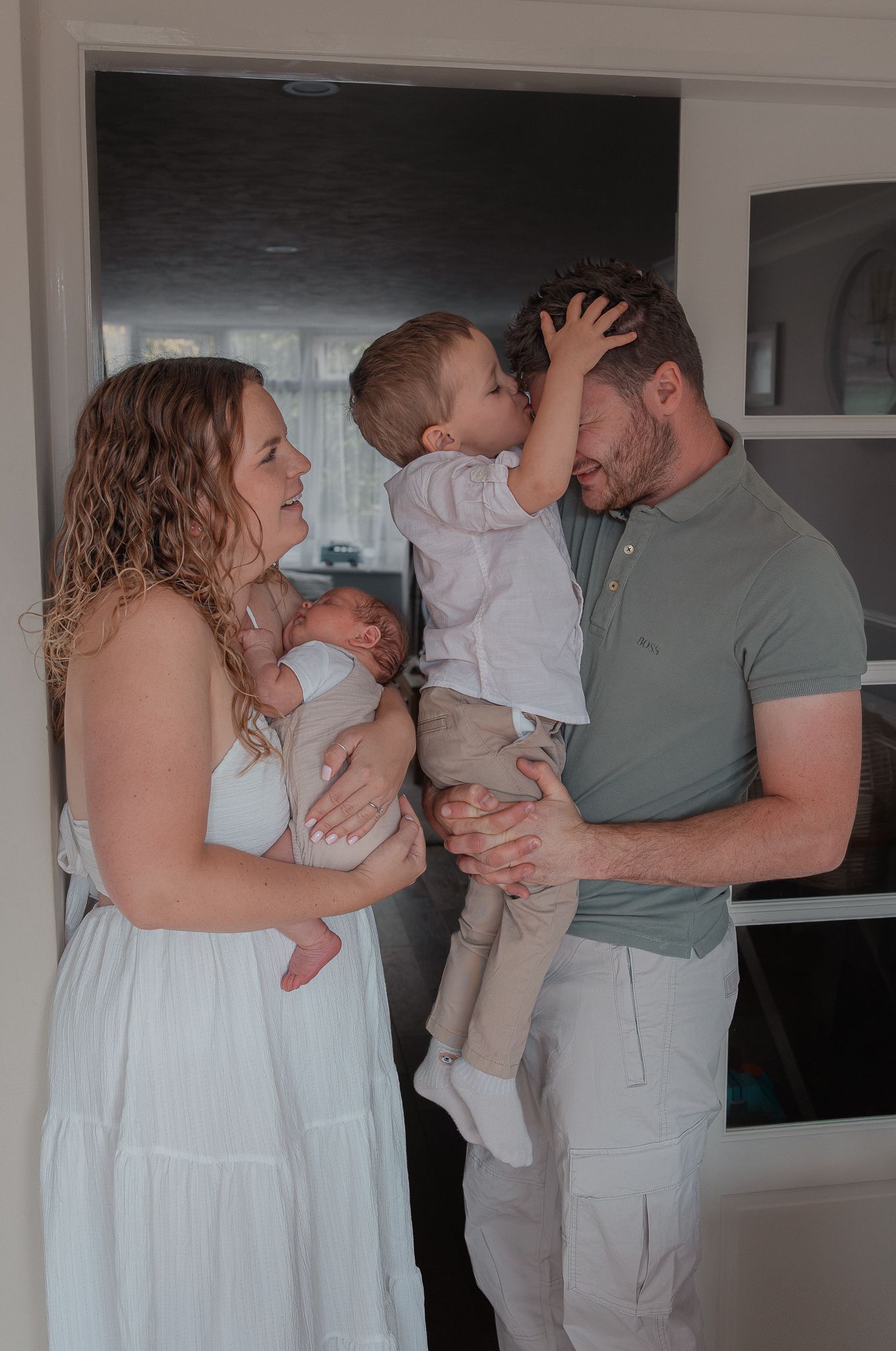 A young family with a newborn baby and toddler share a tender moment in a bright doorway at home in Clevedon, North Somerset.