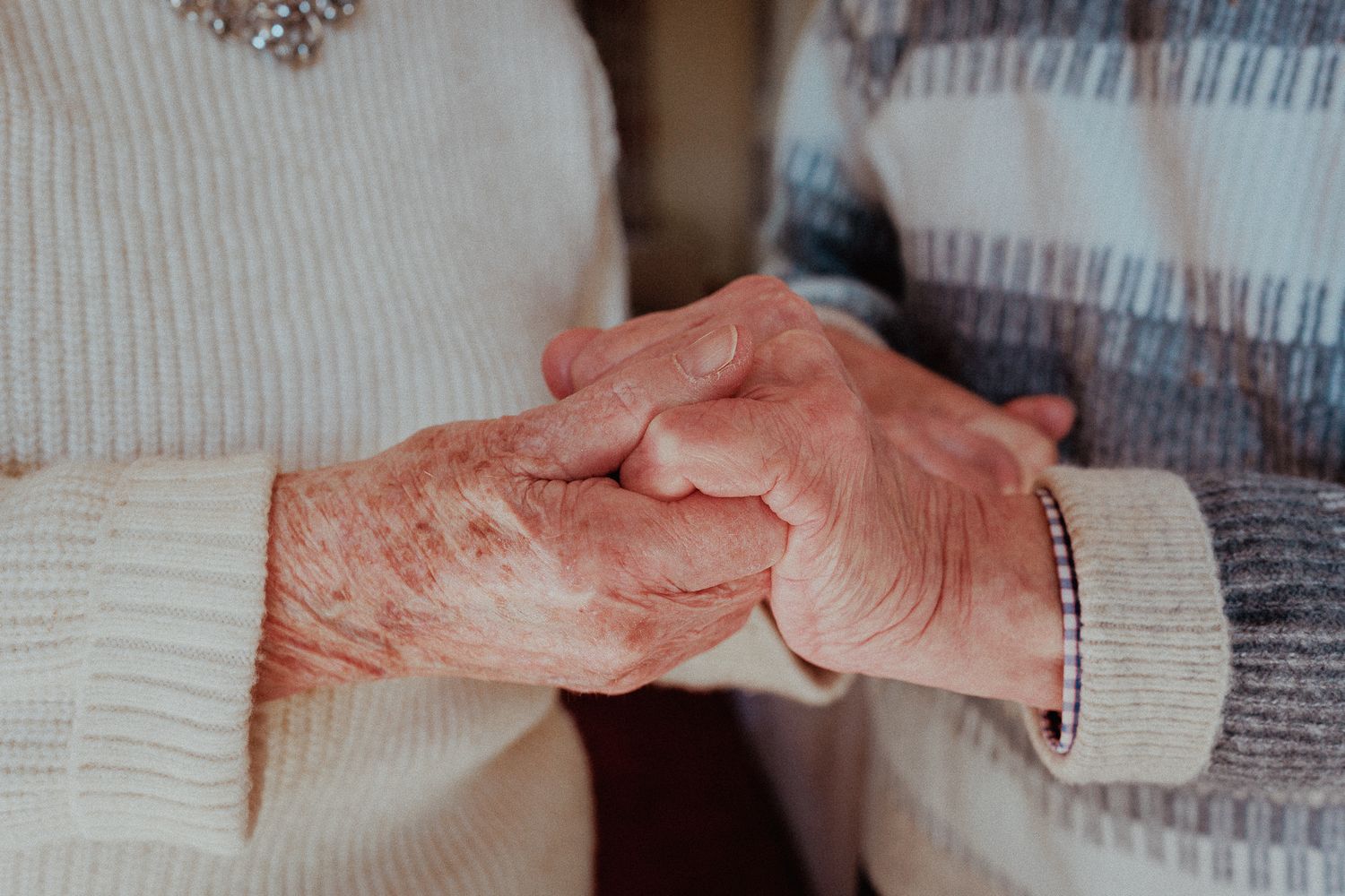 Close-up of two elderly people holding hands tenderly, showing wrinkled skin and a loving bond in Tetbury.