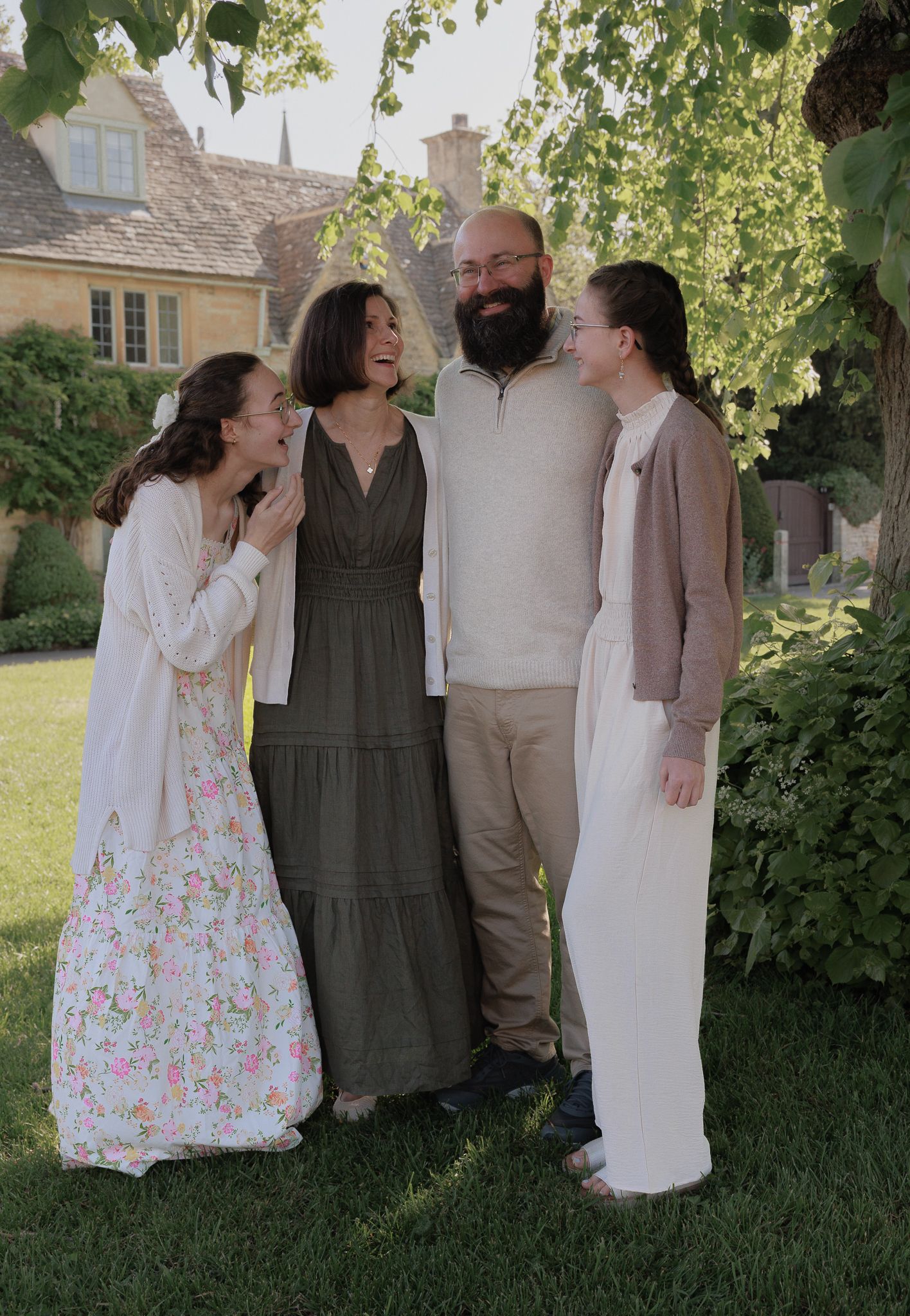 A joyful family of four laughing together outdoors in Lower Slaughter, Cotswolds.