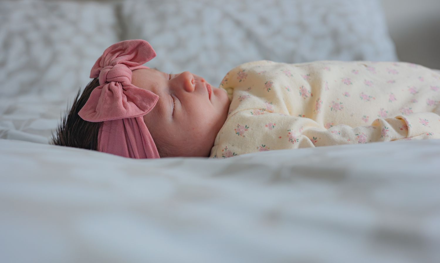 A sleeping newborn baby rests peacefully on white bedding. Upper Slaughter, Cotswolds.