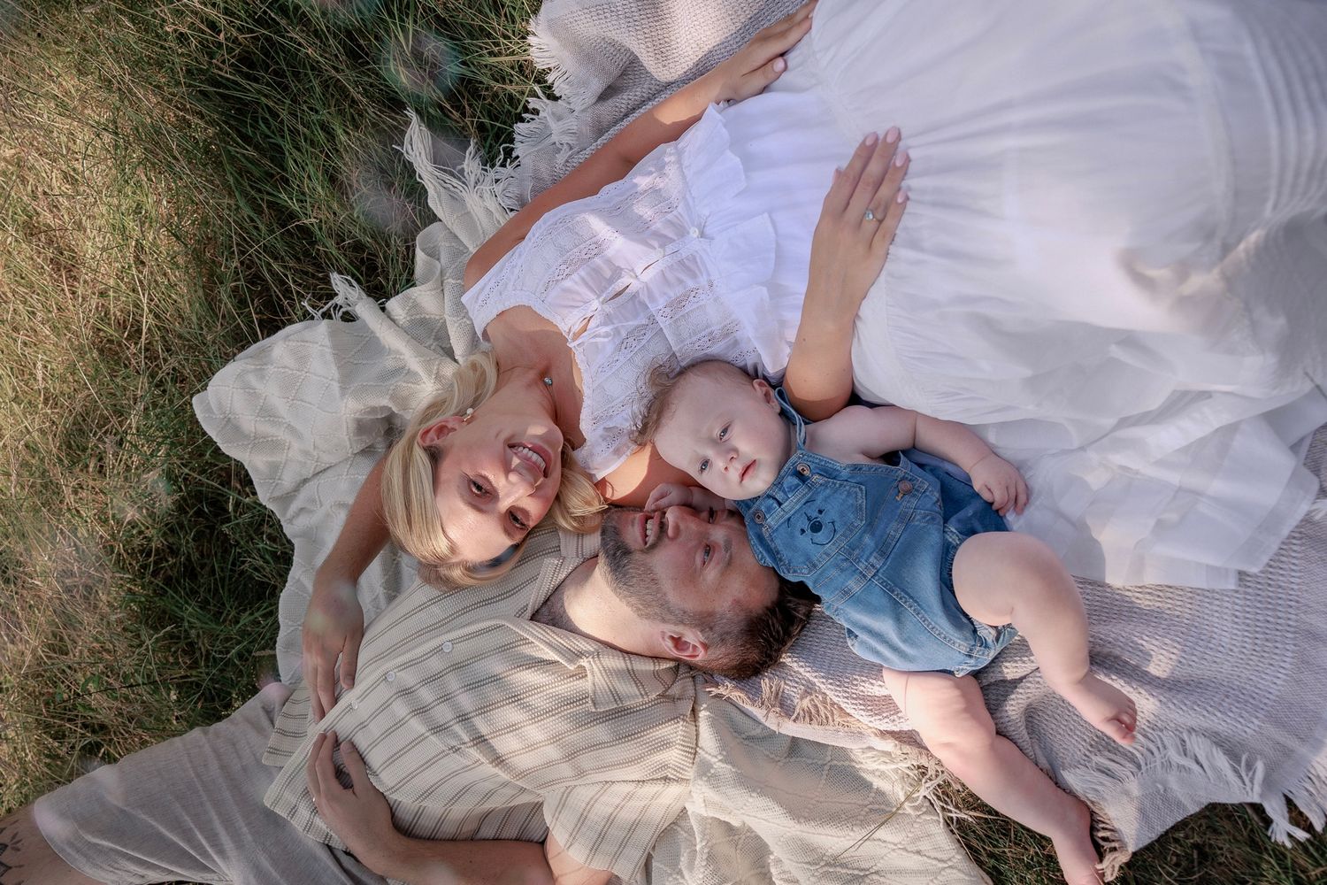 Aerial view of a family with a baby lying on a white blanket in a grassy field in North Cerney, Cotswolds.