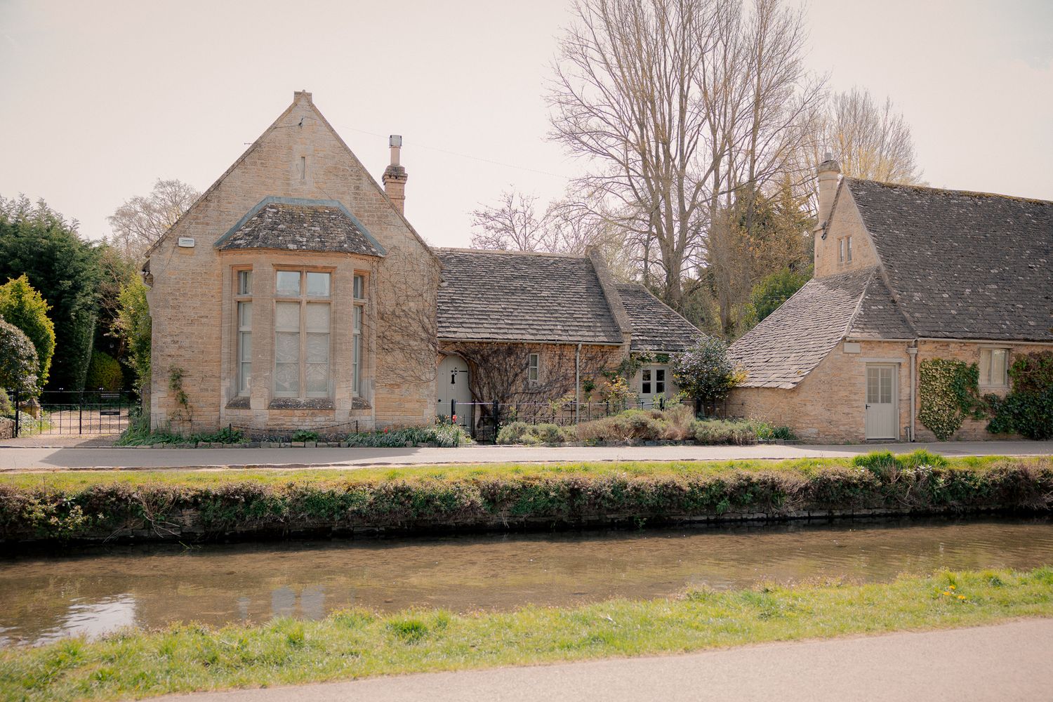Charming Cotswold stone cottages beside a tranquil stream with bare winter trees in an English village in Lower Slaughter, Cotswolds, UK.