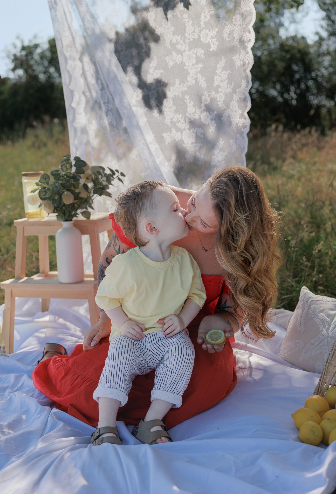 A loving mother in a red dress receives a sweet kiss from her young son at an outdoor picnic in Fairford, Cotswolds.