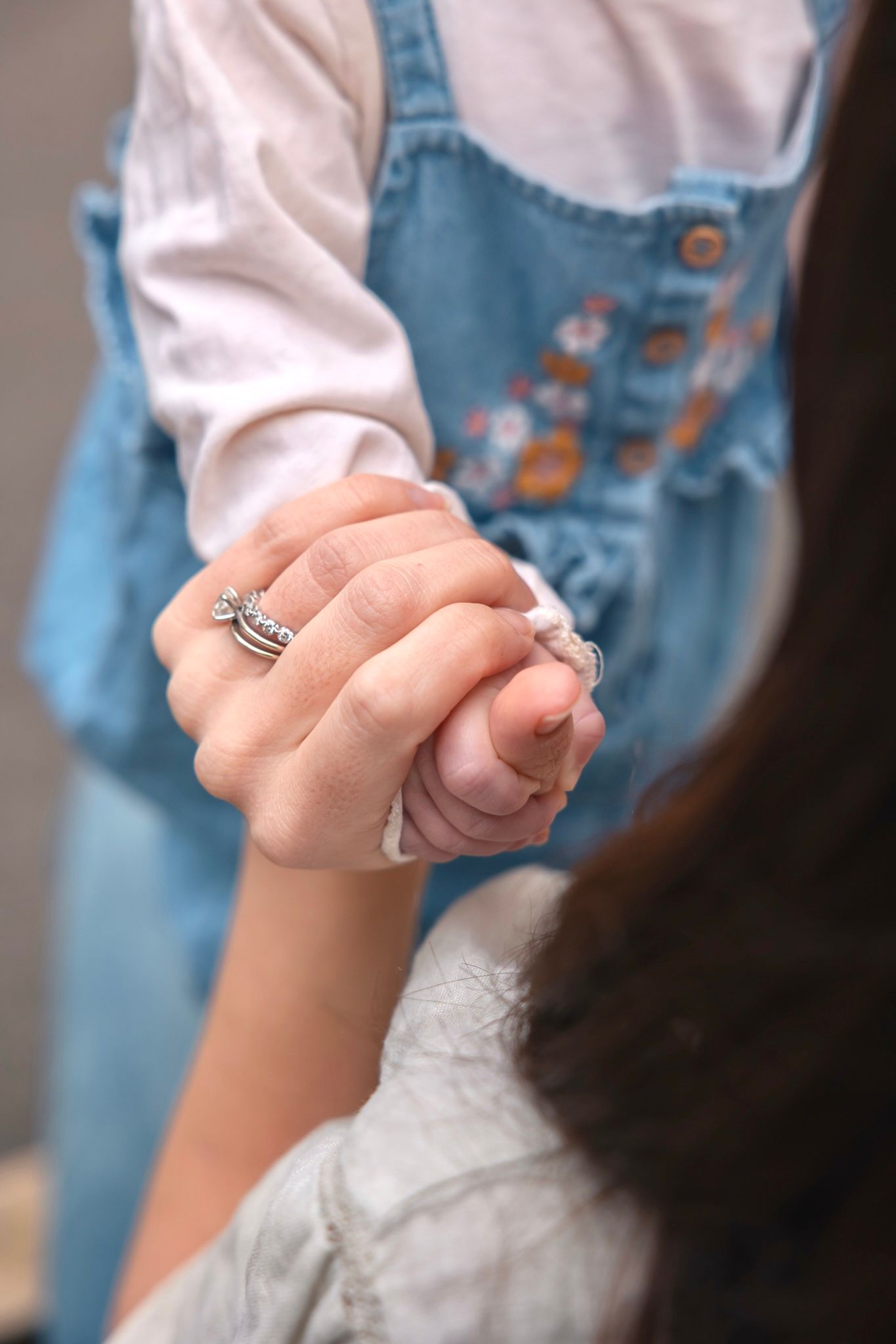 A woman wearing silver rings holds a small child's hand, both dressed in casual clothing in South Cerney, Cotswolds.