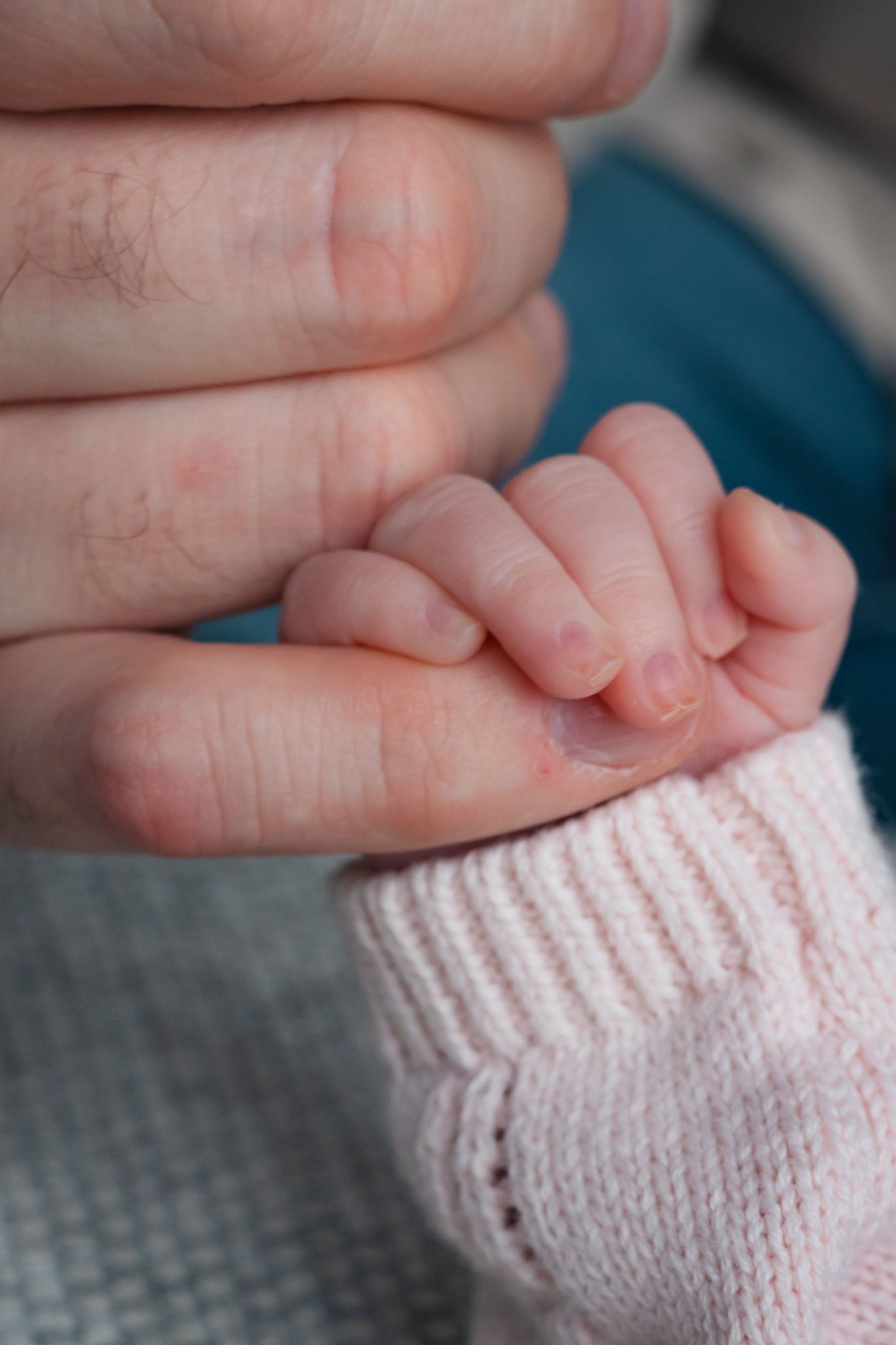 A close-up photograph showing tiny newborn baby hands gently wrapped around mothers pinky finger. Marlborough, Wiltshire.