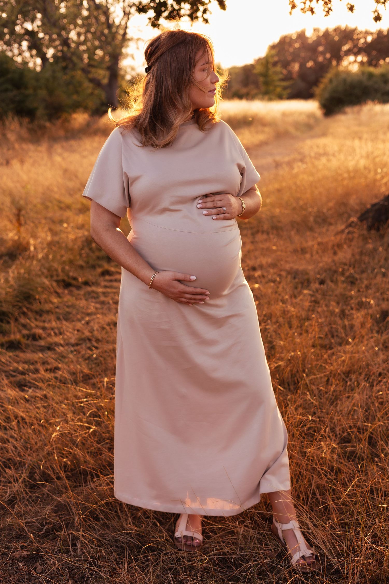 Maternity photos at sunset with woman in pink dress touching her belly. Golden Hour Photoshoot in Bourton-On-The-Water