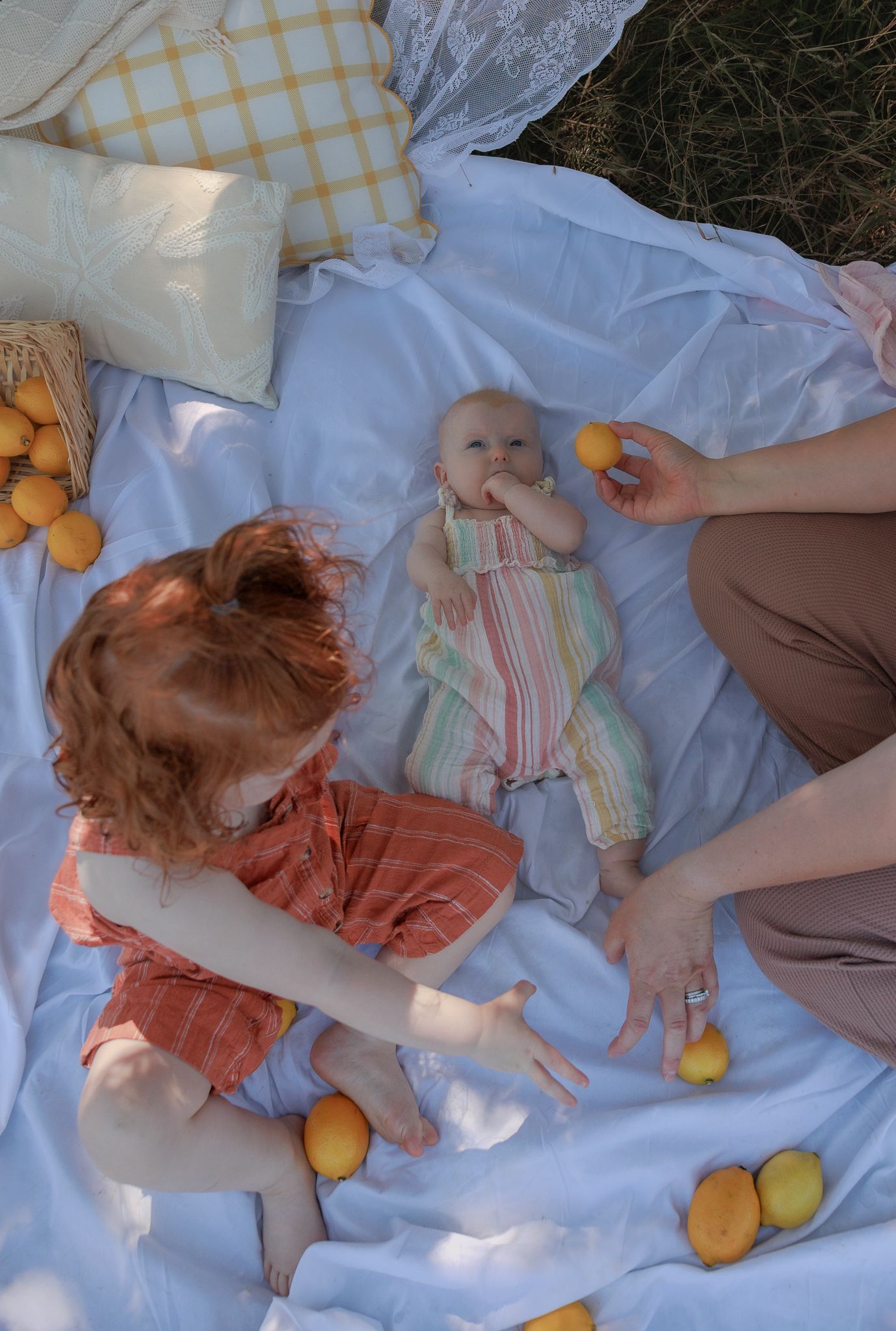 A toddler and baby enjoy a sunny picnic on a white blanket surrounded by fresh lemons in Henley-on-Thames, Oxfordshire.