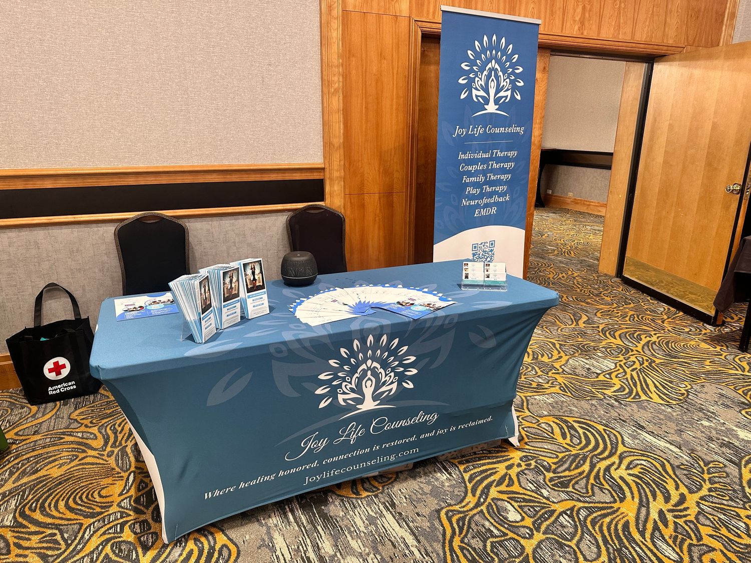 Joy Life Counseling branded display booth with teal tablecloth, brochures, and pull-up banner at a professional event.