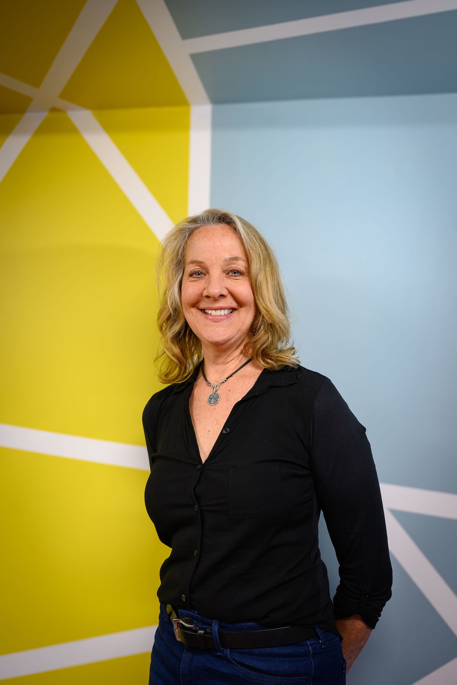 Smiling woman in black shirt standing in front of colorful geometric painted wall.
