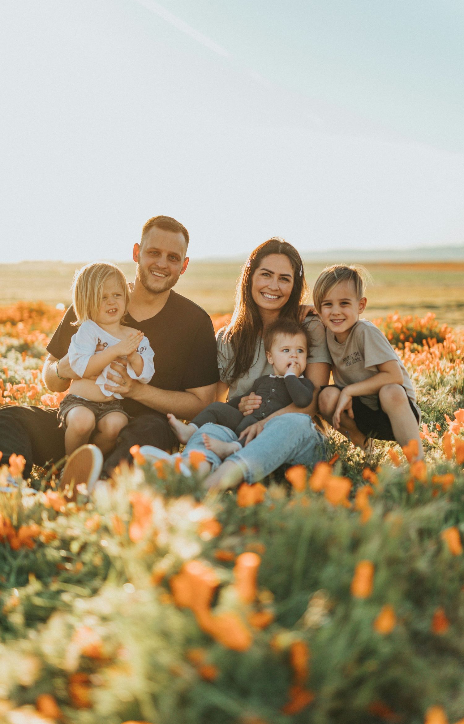 Happy family of five sitting in a vibrant field of orange wildflowers during golden hour.