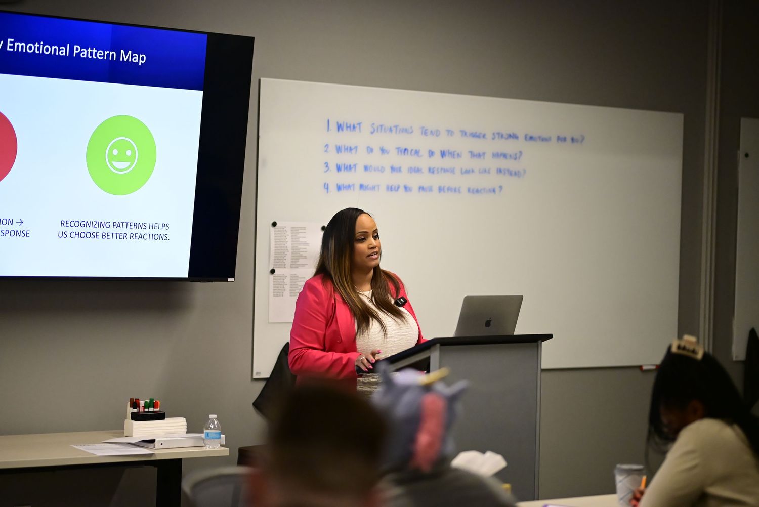 A woman in a red blazer speaks at a podium beside a projected Emotional Pattern Map.