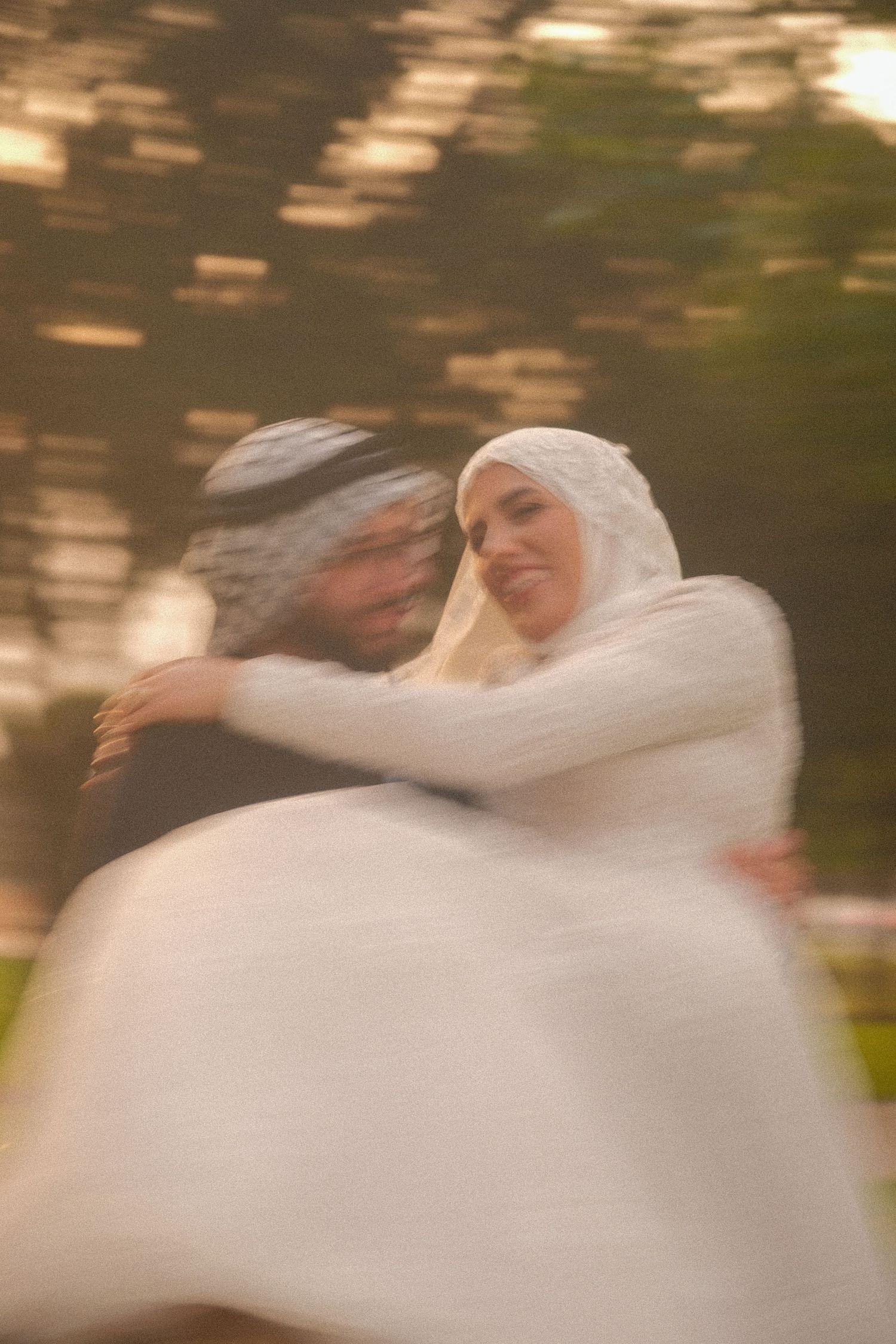 Blurry motion photo of Muslim wedding couple embracing, bride in white hijab and groom in keffiyeh outdoors.