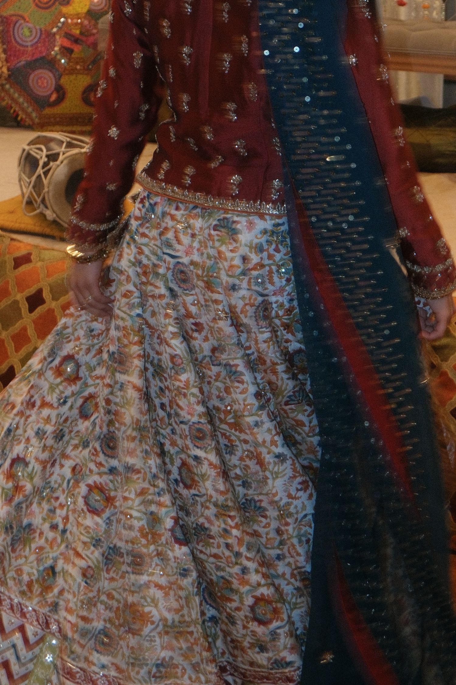 A woman wearing a traditional embroidered maroon and white floral lehenga with a navy blue dupatta at an Indian wedding.