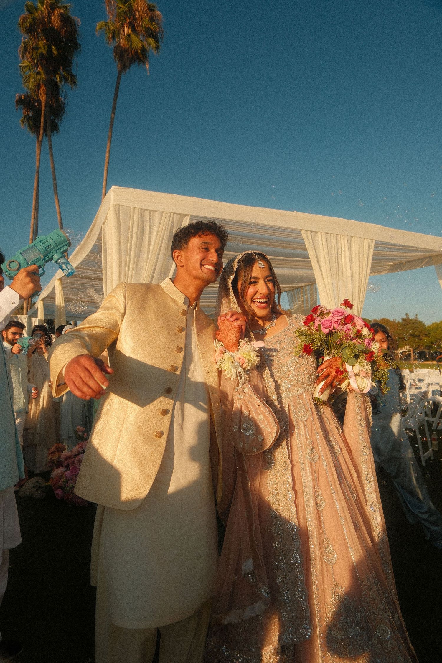 Joyful Pakistani bride and groom in traditional attire celebrating after outdoor nikah wedding ceremony.