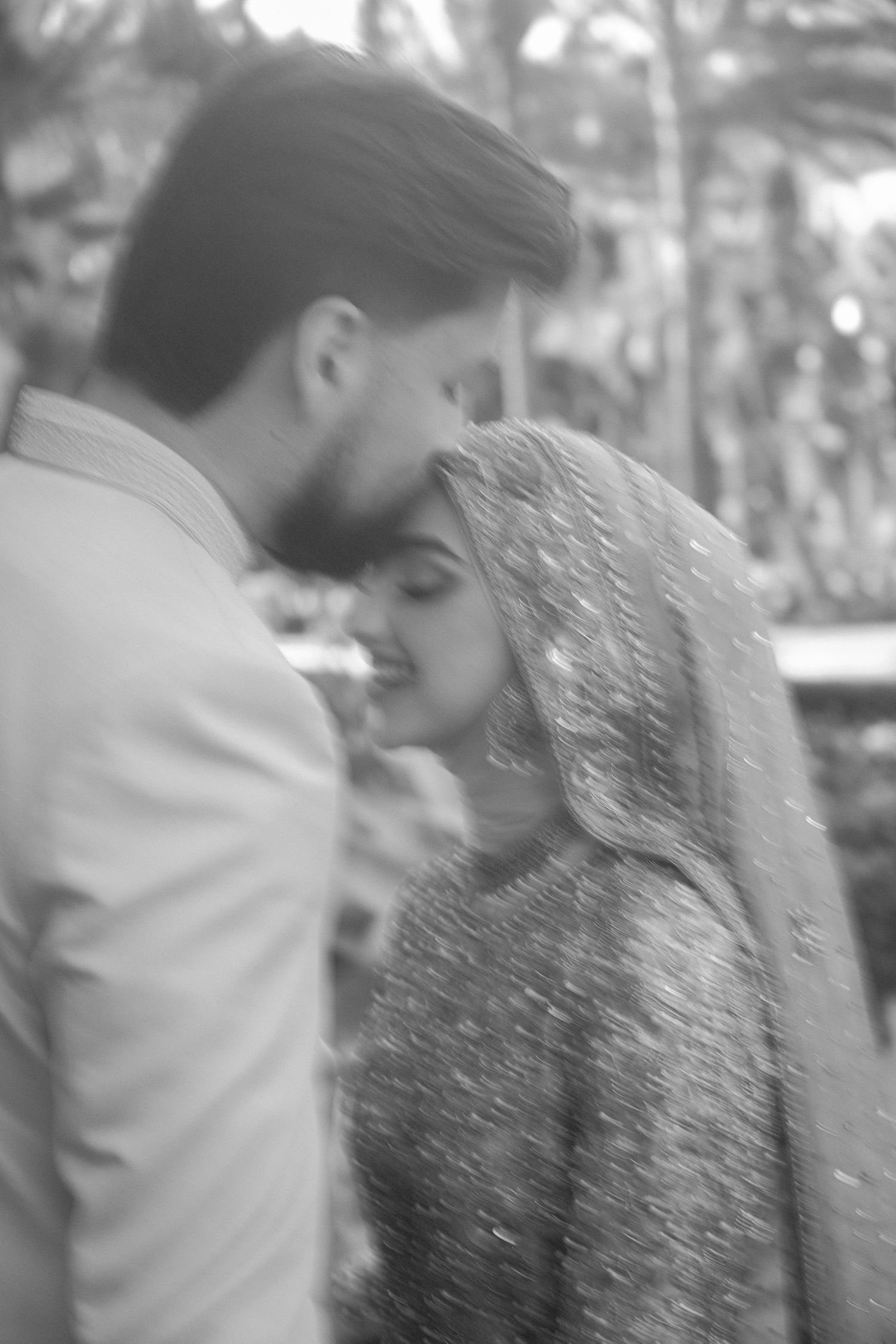 Black and white romantic close-up of South Asian couple sharing tender moment under veil.