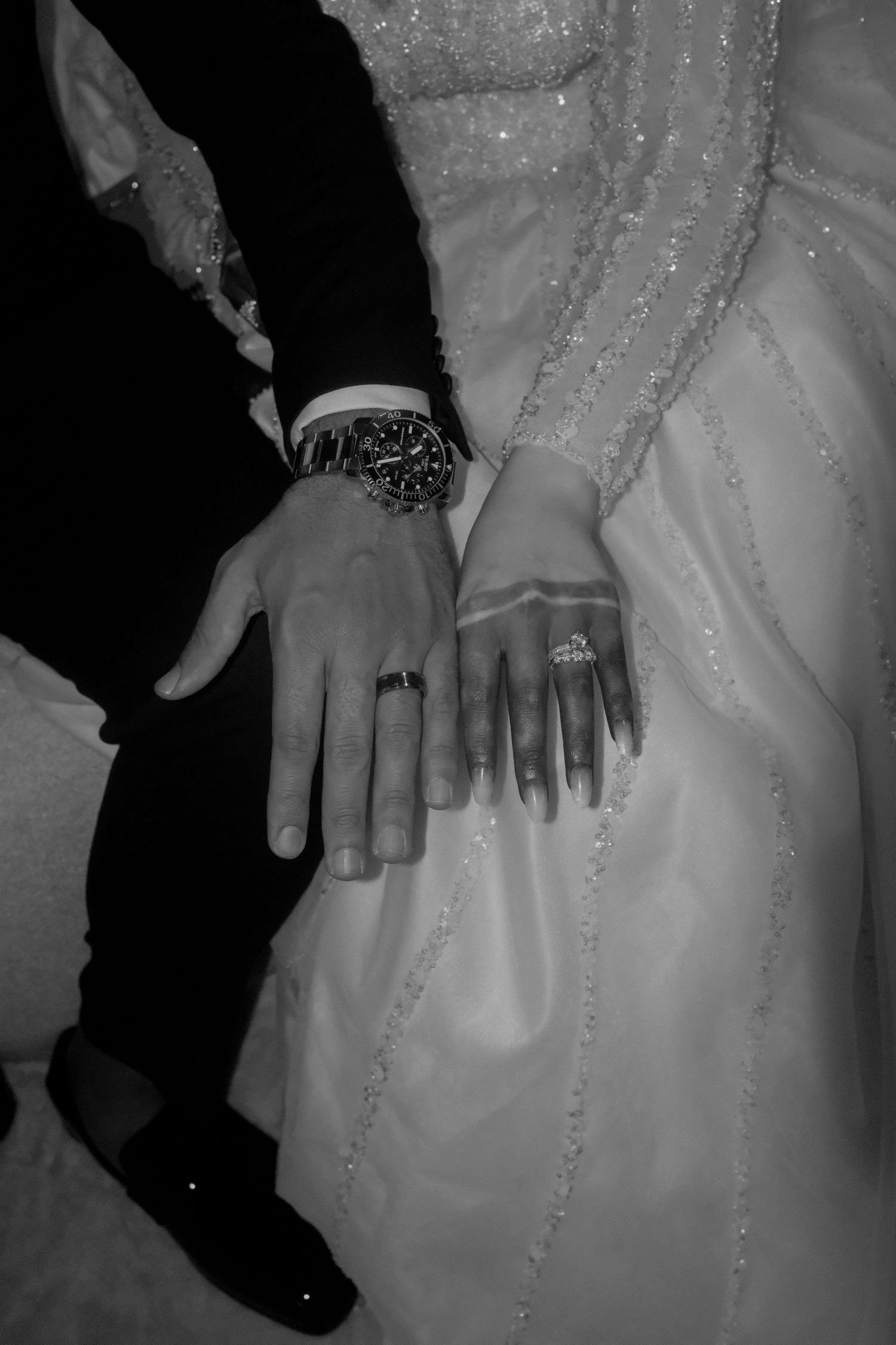 Black and white photo of newlyweds displaying wedding rings, groom wearing a luxury watch.