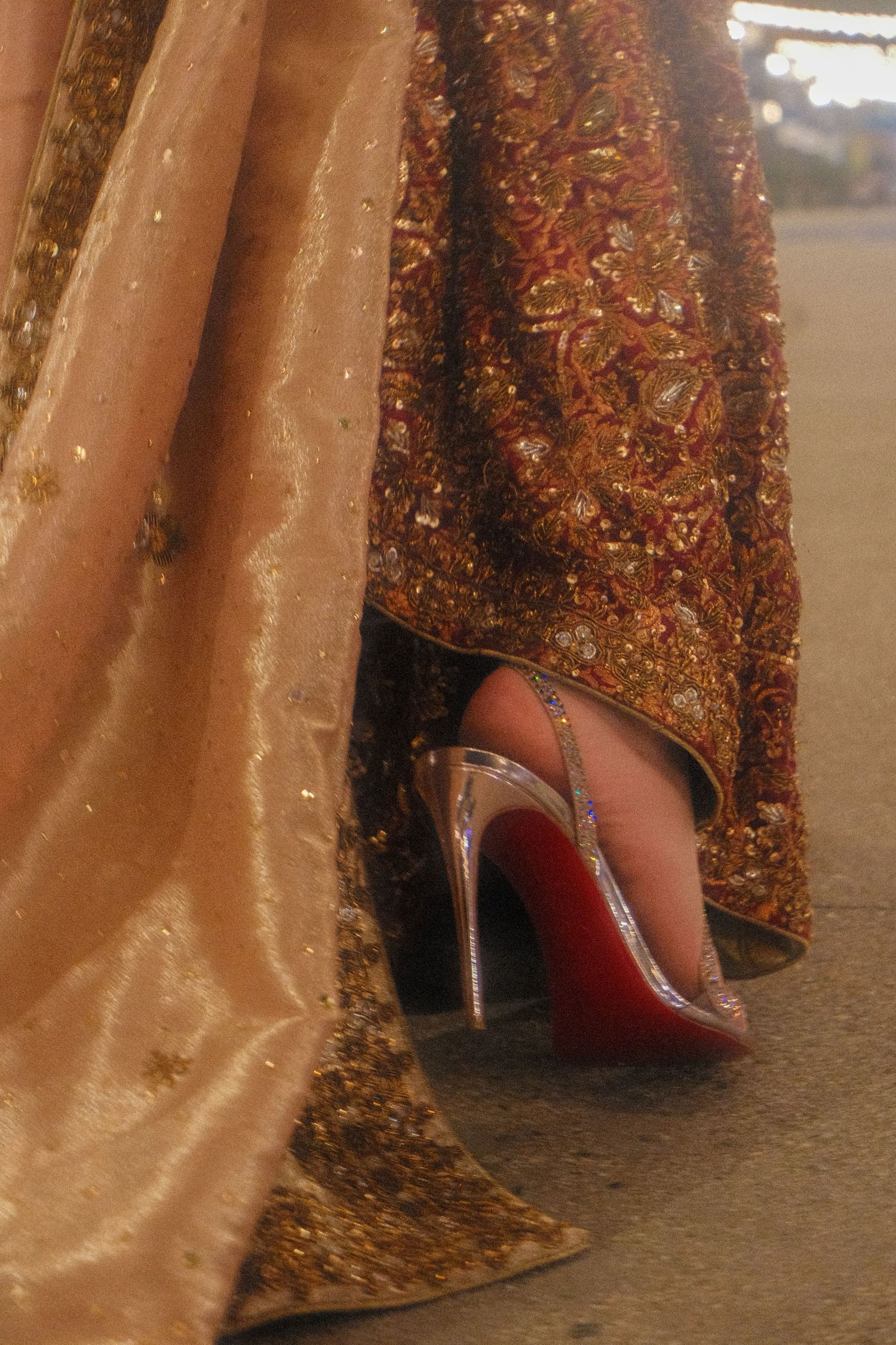 Bride wearing Christian Louboutin silver heels beneath elaborate gold and red embroidered bridal lehenga.