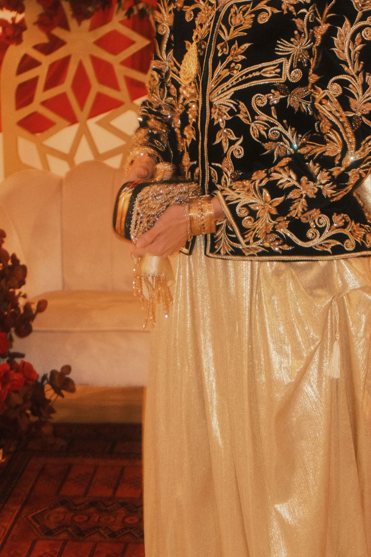 A person wearing an elaborately embroidered black and gold traditional jacket with shimmering gold pants.
